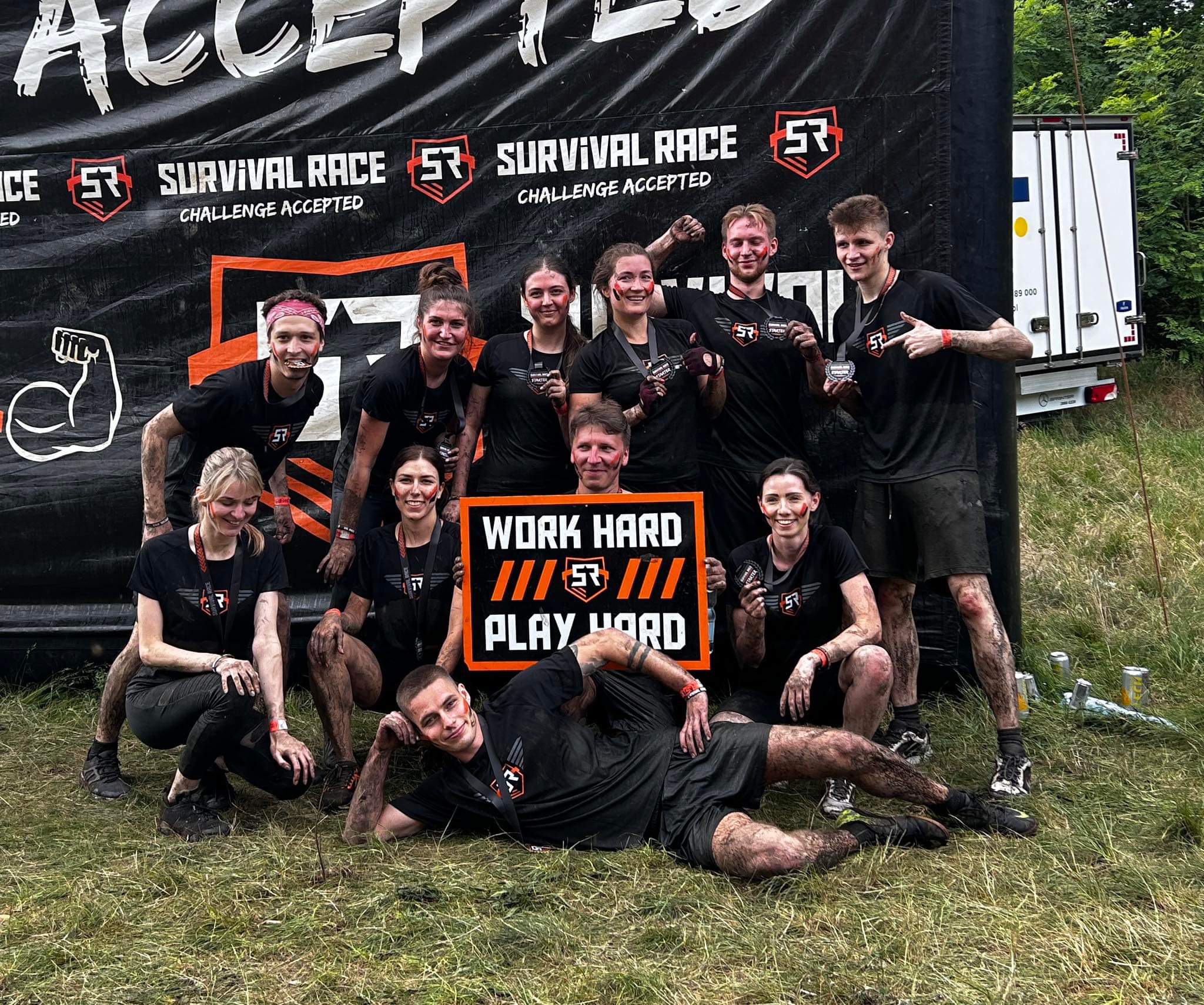 Egala by Boekestijn team after completing a muddy obstacle run, holding a ‘Work Hard Play Hard’ sign — celebrating teamwork, resilience, and strong company spirit.