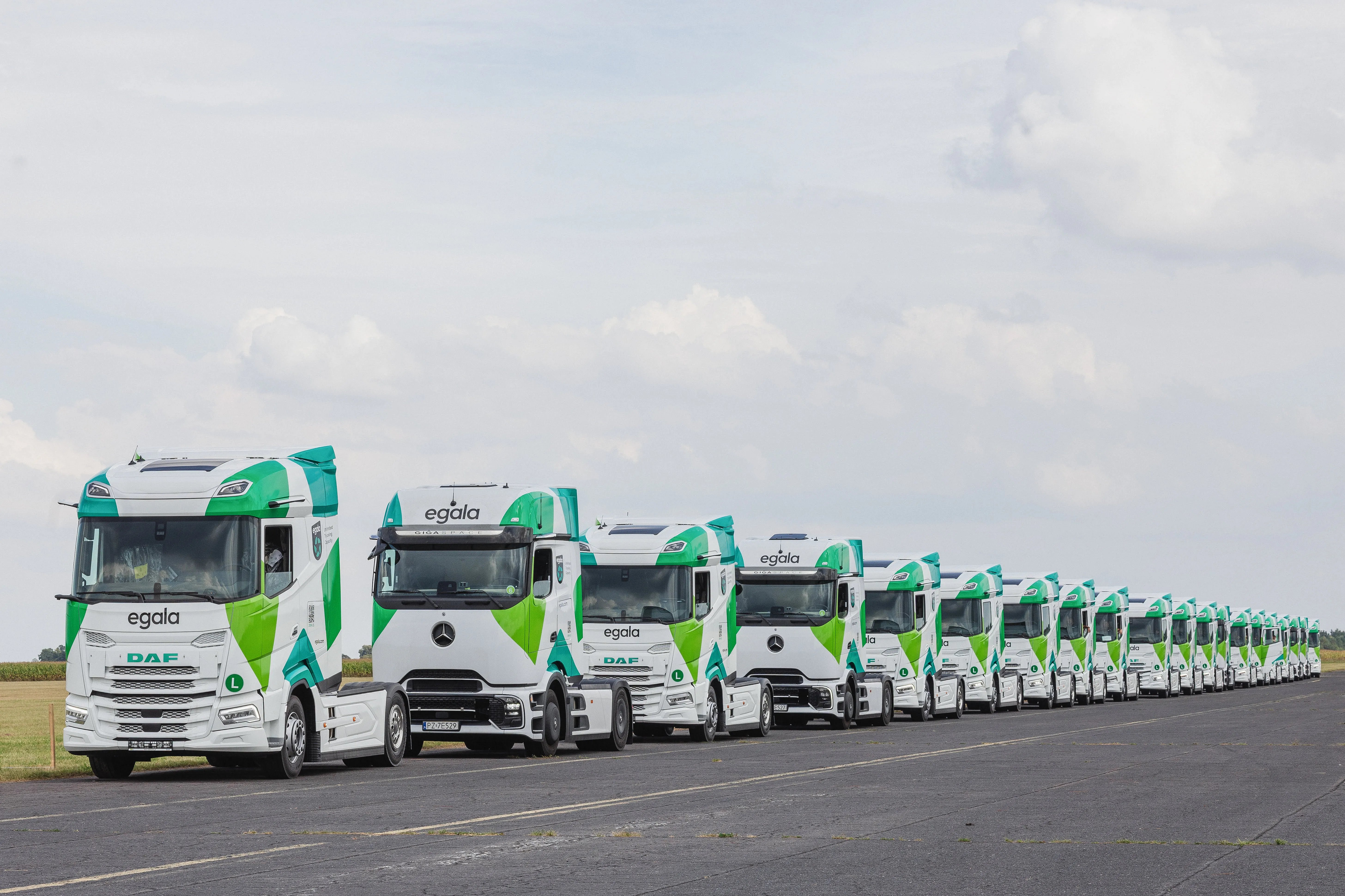 Row of Egala by Boekestijn green and white trucks parked in formation on an open lot.