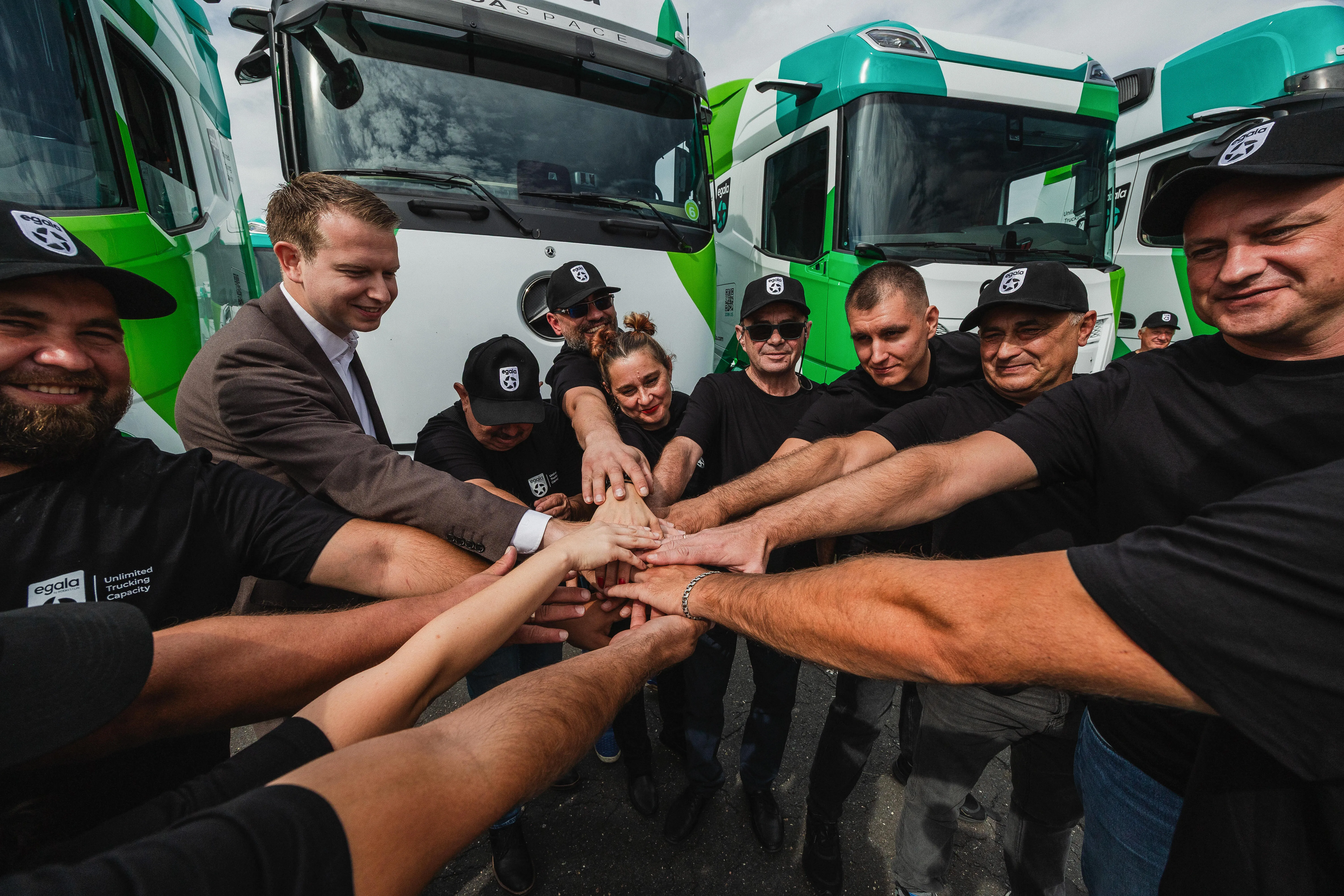 Egala by Boekestijn drivers forming a team huddle with hands stacked together in front of company trucks.
