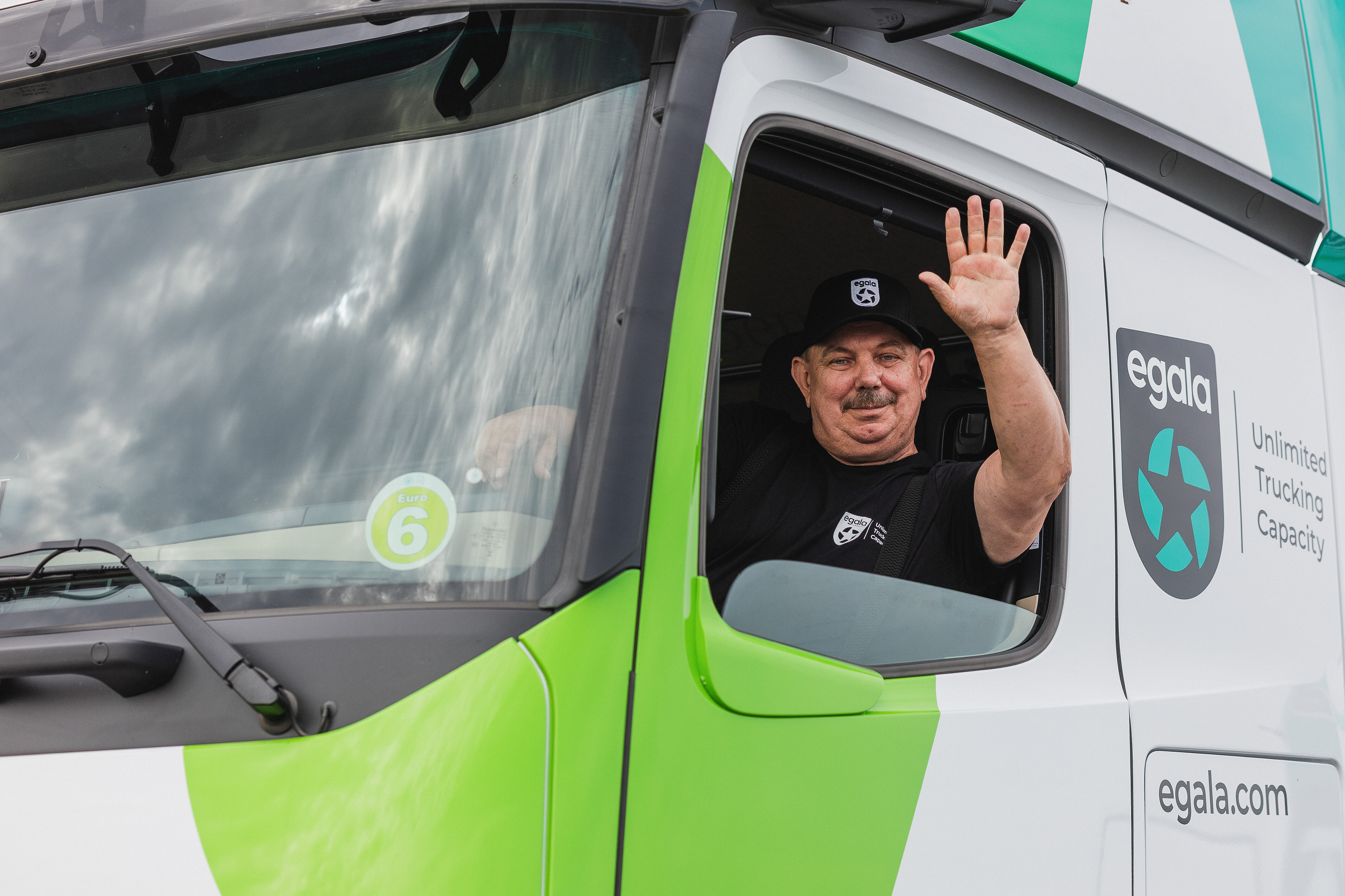 Egala by Boekestijn driver smiling and waving from the cab window of a green and white truck.