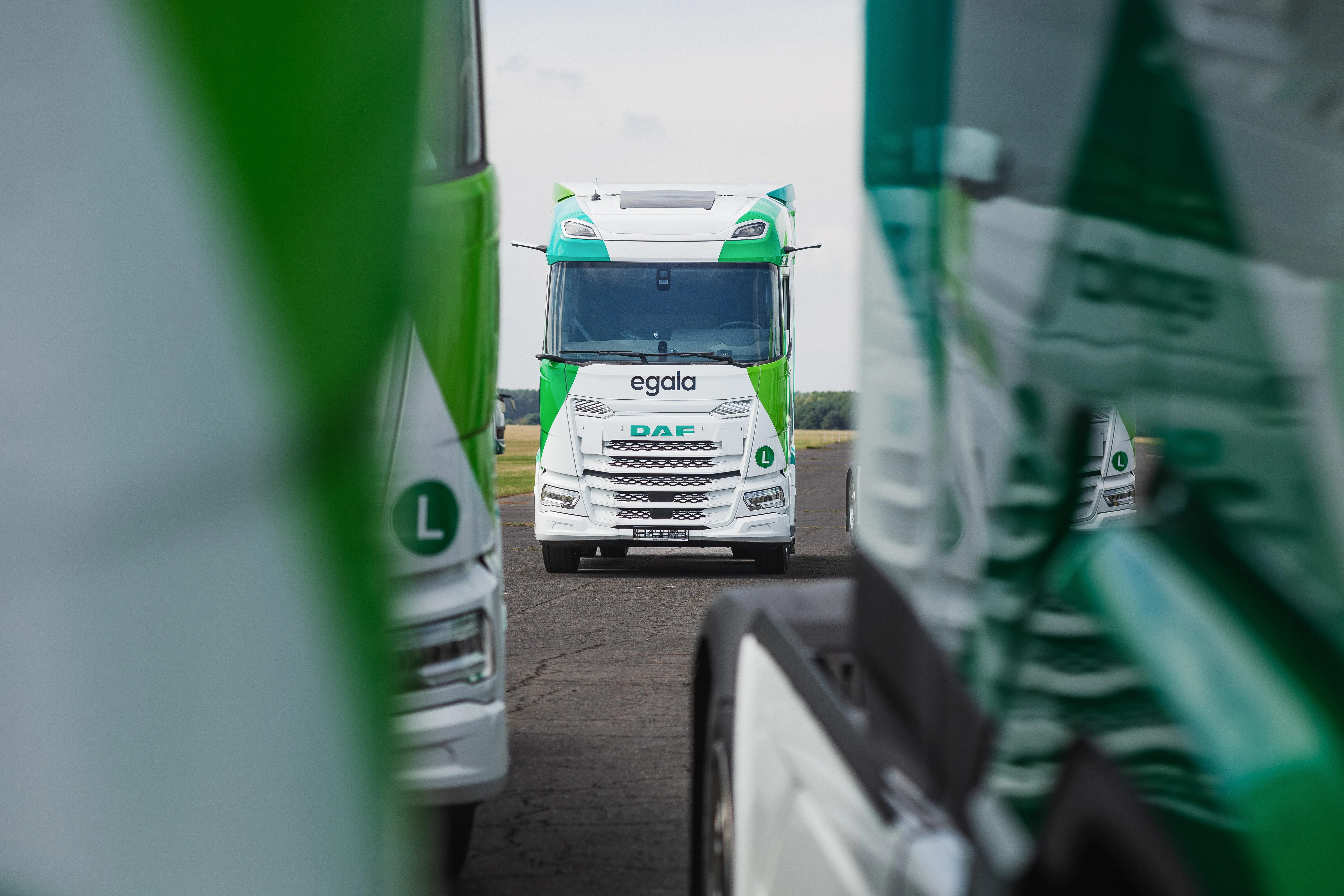 A green and whiteEgala  truck seen head-on, framed between two other trucks, highlighting the company’s modern fleet.