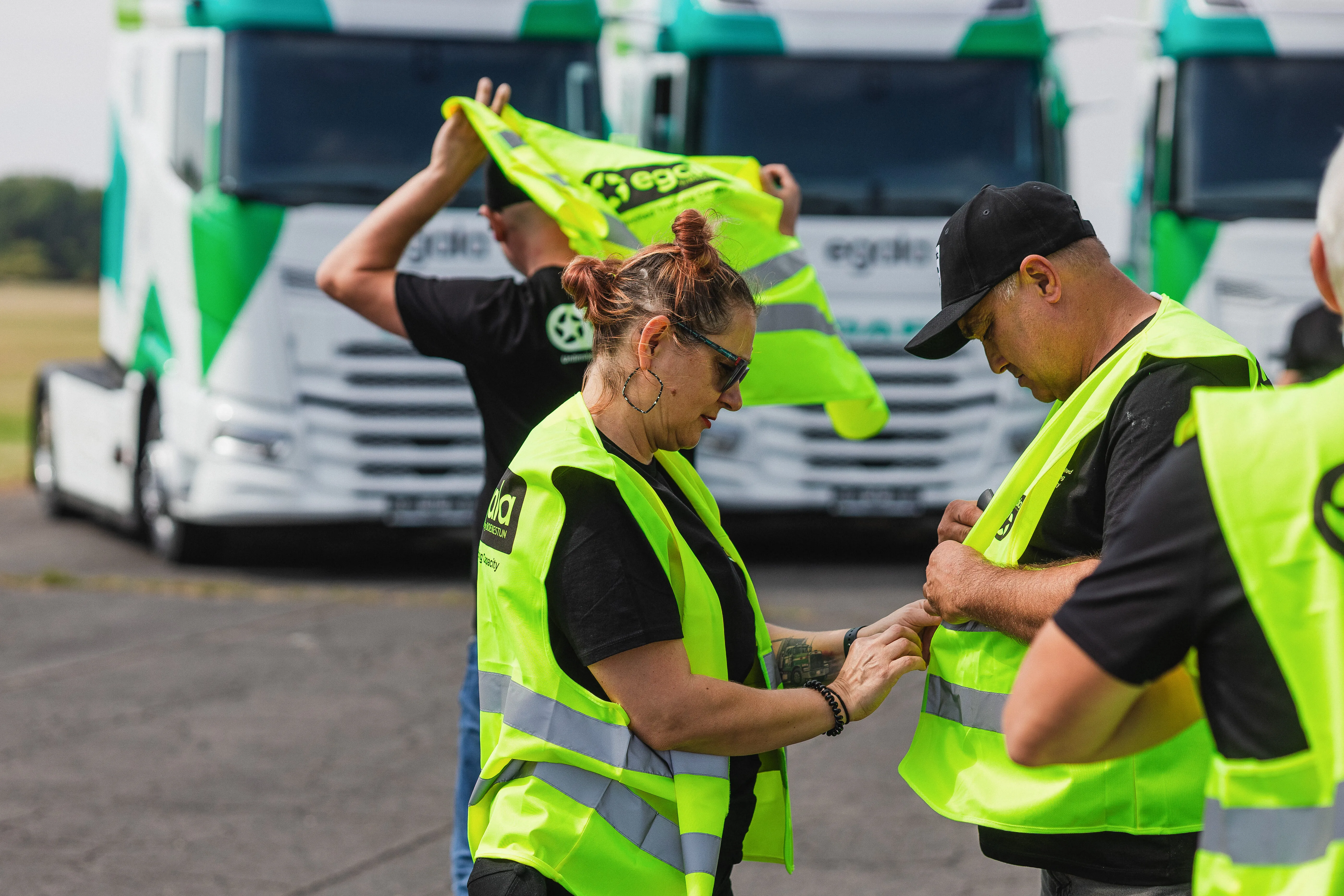 Egala by Boekestijn truck drivers helping each other with safety vests in front of green and white trucks — promoting teamwork and safety in European trucking.