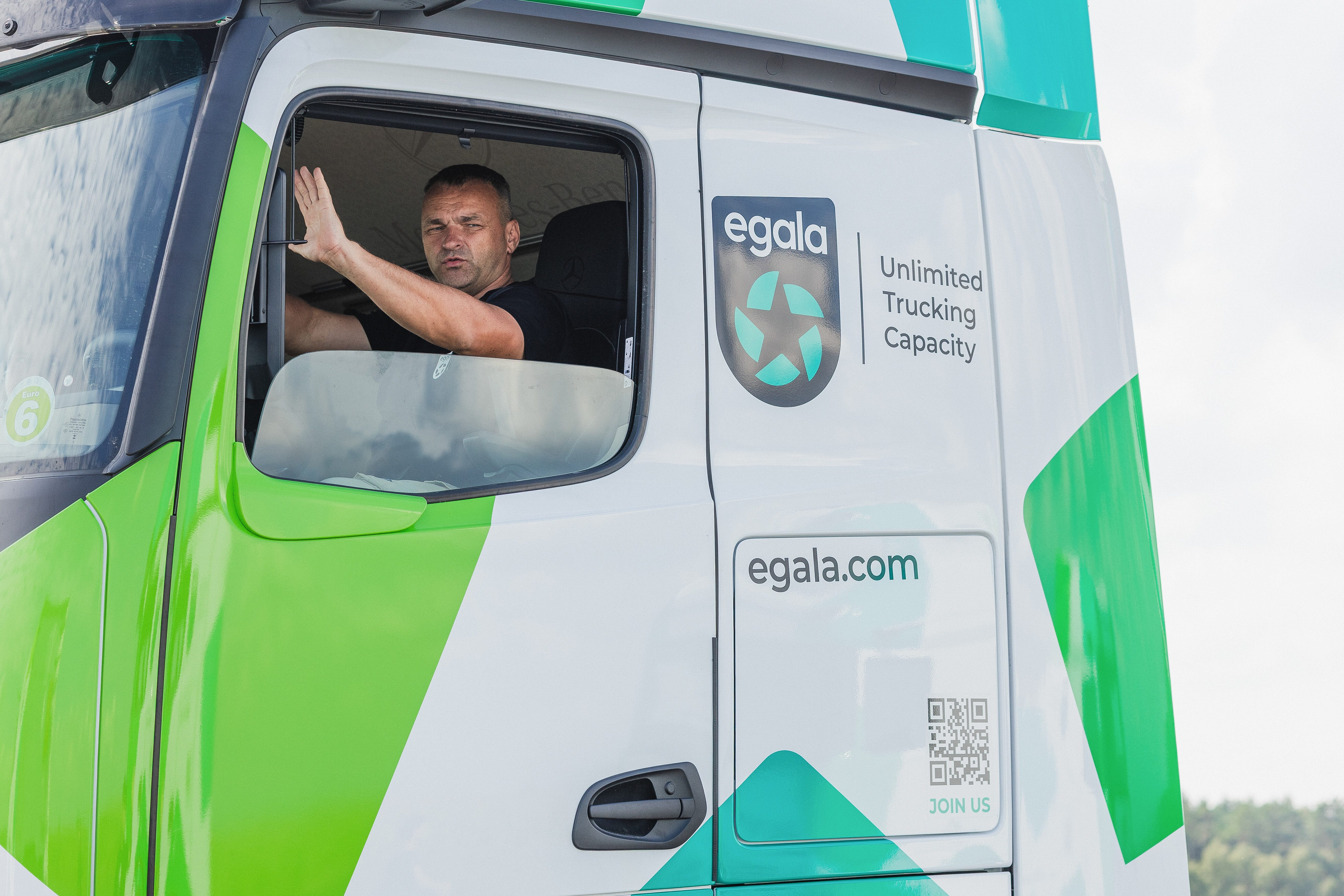 Egala by Boekestijn driver waving from the cab window of a green and white truck.