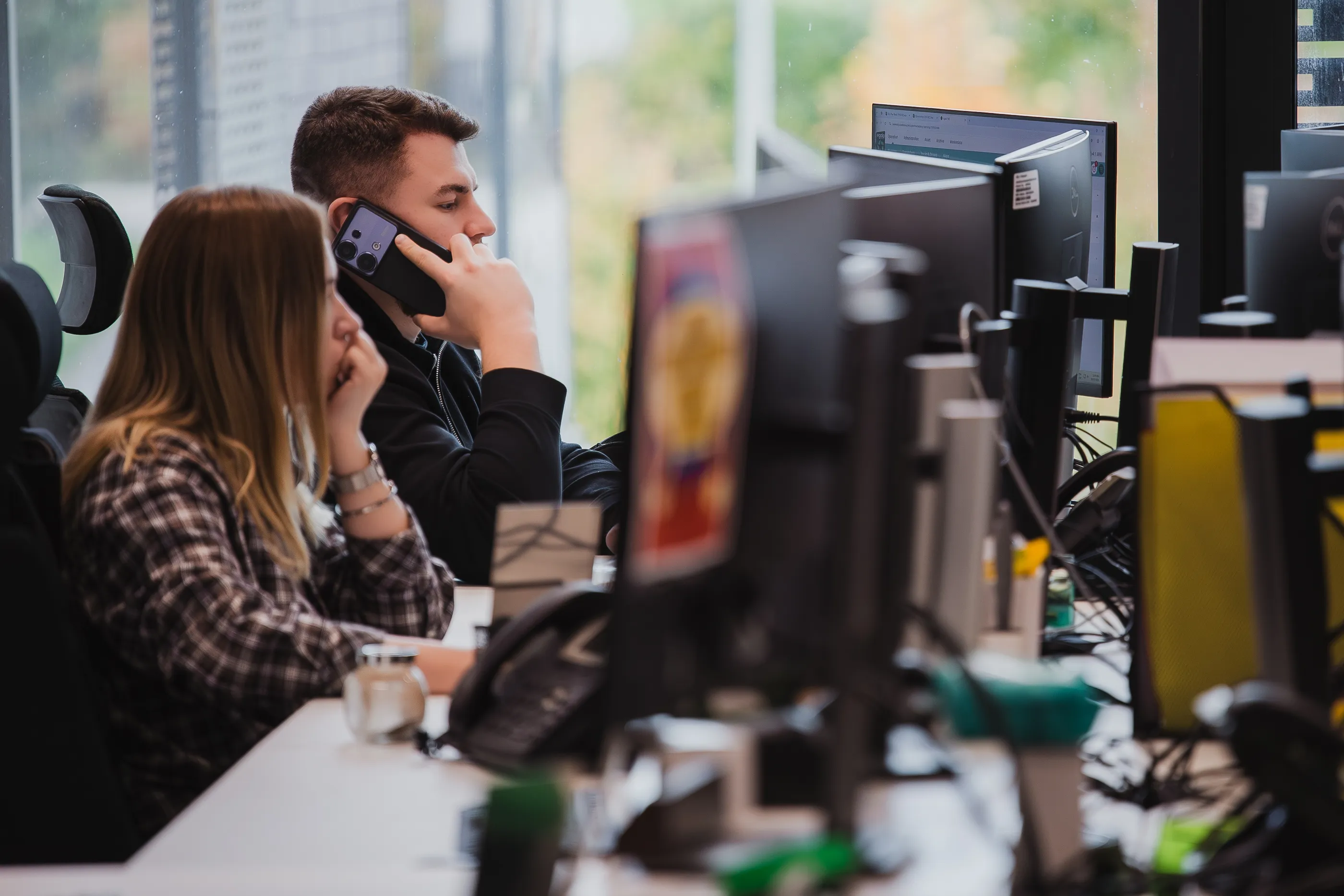 Customer service coordinator at Egala by Boekestijn speaking on the phone while managing logistics and transport operations at a computer workstation in a modern office.