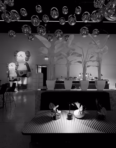 Modern indoor space with a striped table, decorative plants, hanging glass orbs, and large cartoon-like statues in the background.