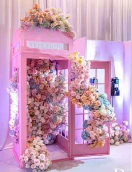 Pink vintage telephone booth decorated with cascading pastel-colored flowers inside and on top.