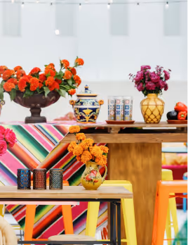 Colorful festive table setup with vibrant flowers in vases, decorative candles, and a striped tablecloth under string lights.