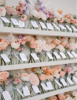 Shelves with glass bottles holding pastel-colored flowers and attached white name tags.