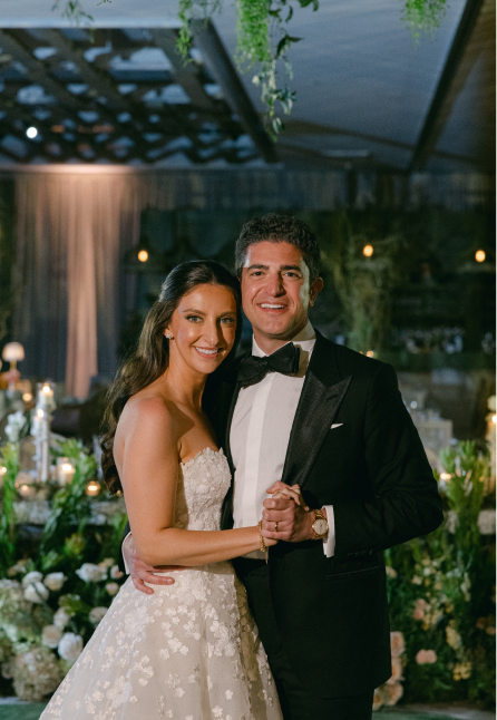 Smiling bride in white strapless gown and groom in black tuxedo dancing at a decorated wedding reception.