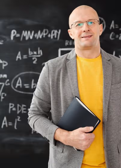 Bald man wearing glasses, a yellow shirt, and a gray blazer holding a notebook with a blackboard full of math formulas in the background.