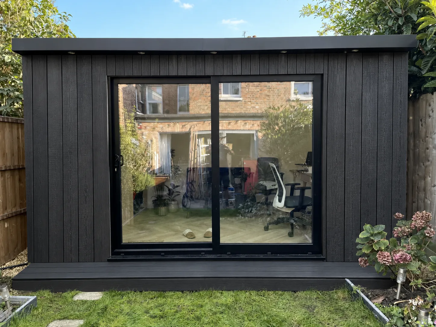 Black-clad garden office with large sliding glass doors and a desk inside
