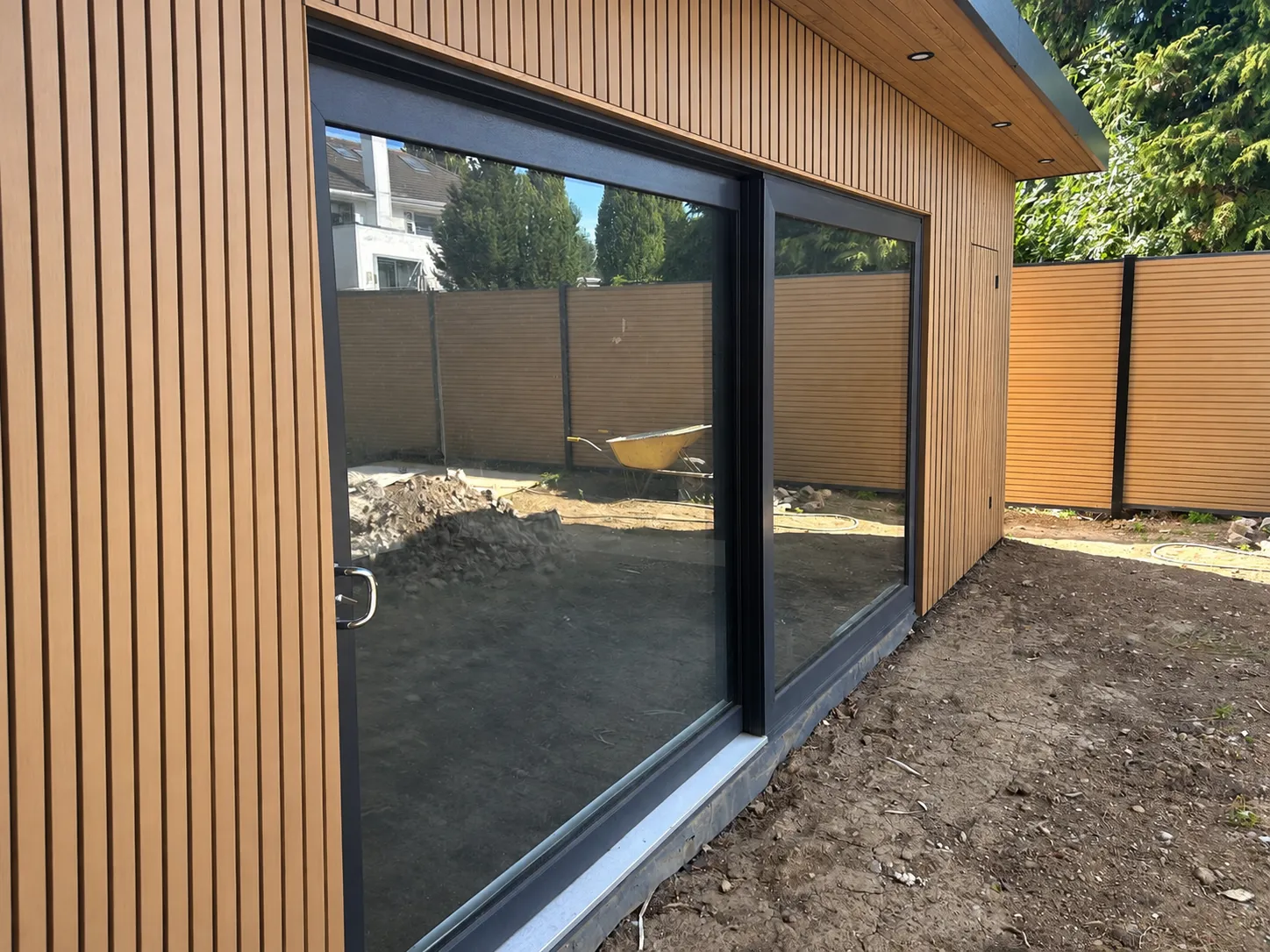 Garden room under construction with timber-effect composite cladding and aluminium sliding doors