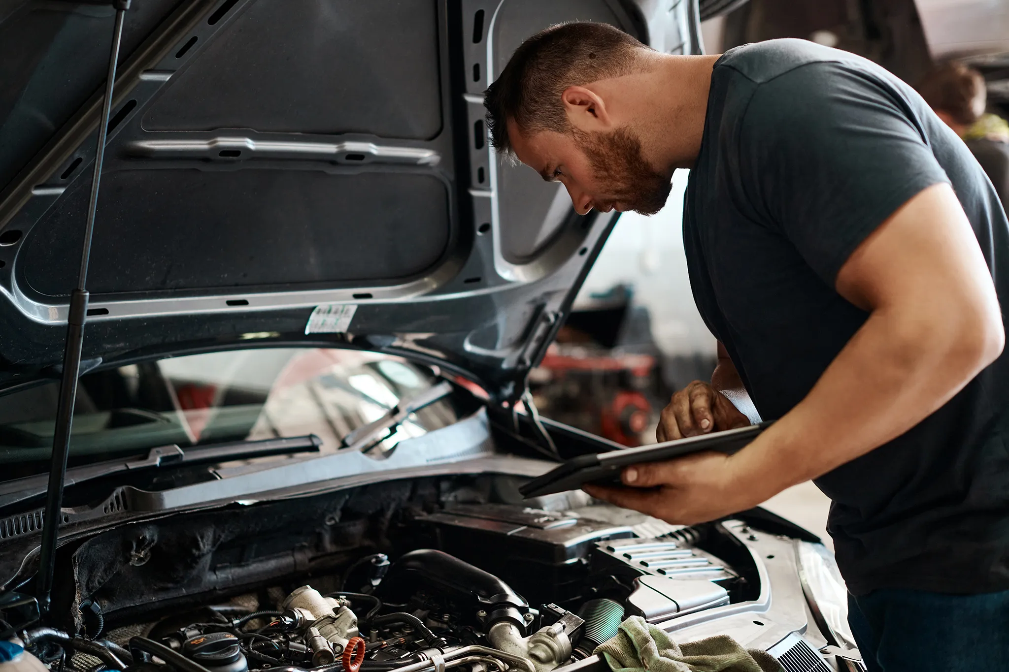 Mechanic leaning over the enging of a vehicle with tablet in his hands