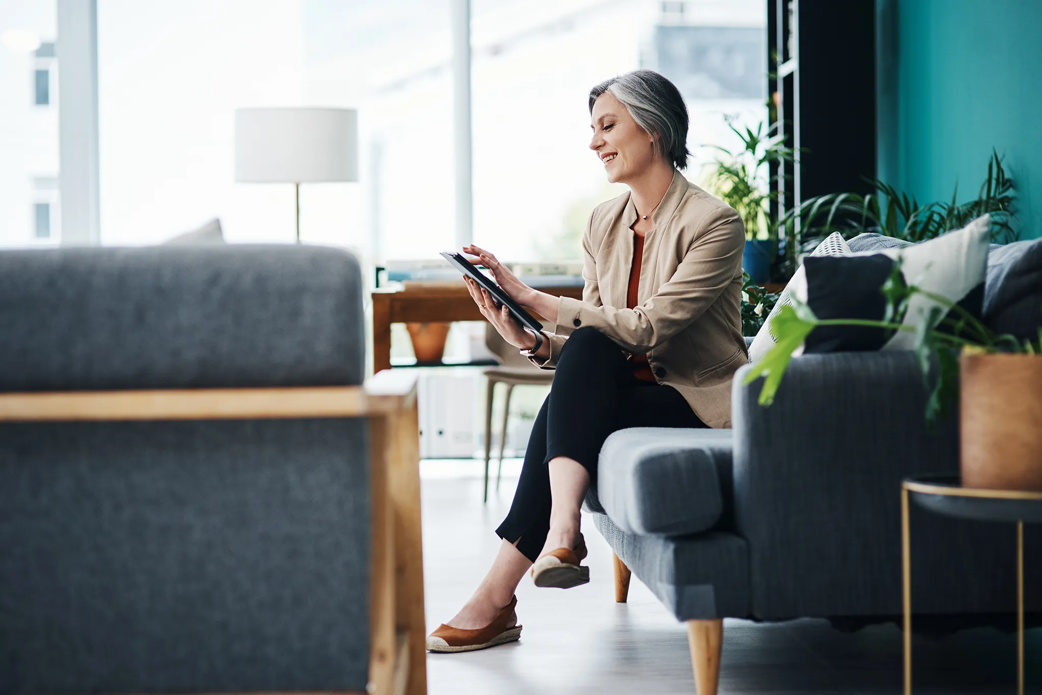 Mature businesswoman sitting on a couch smiling while working on her tablet
