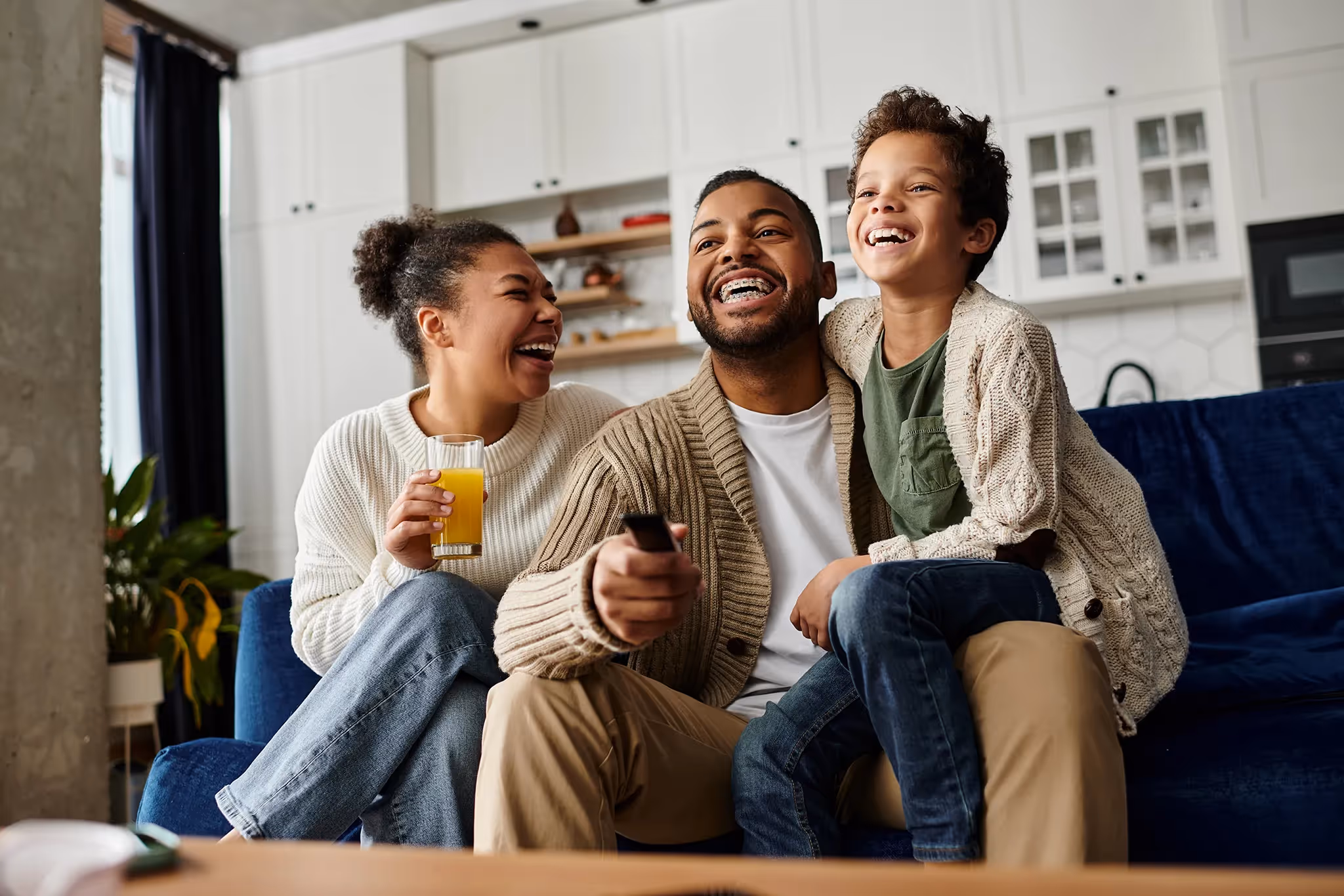 happy healthy young mother, father and young child sitting on blue couch laughing