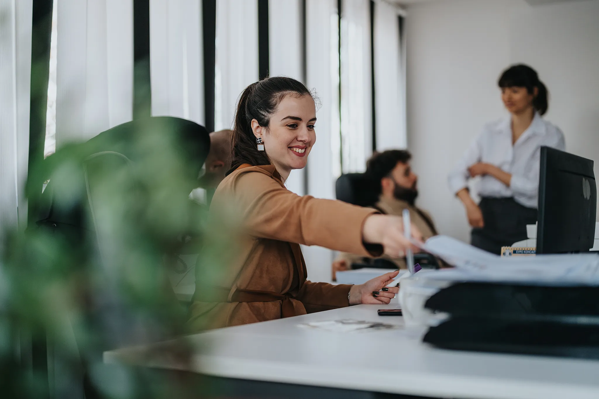 Smiling young woman sitting at her desk placing a paper in her outbox with two of her colleagues in the background
