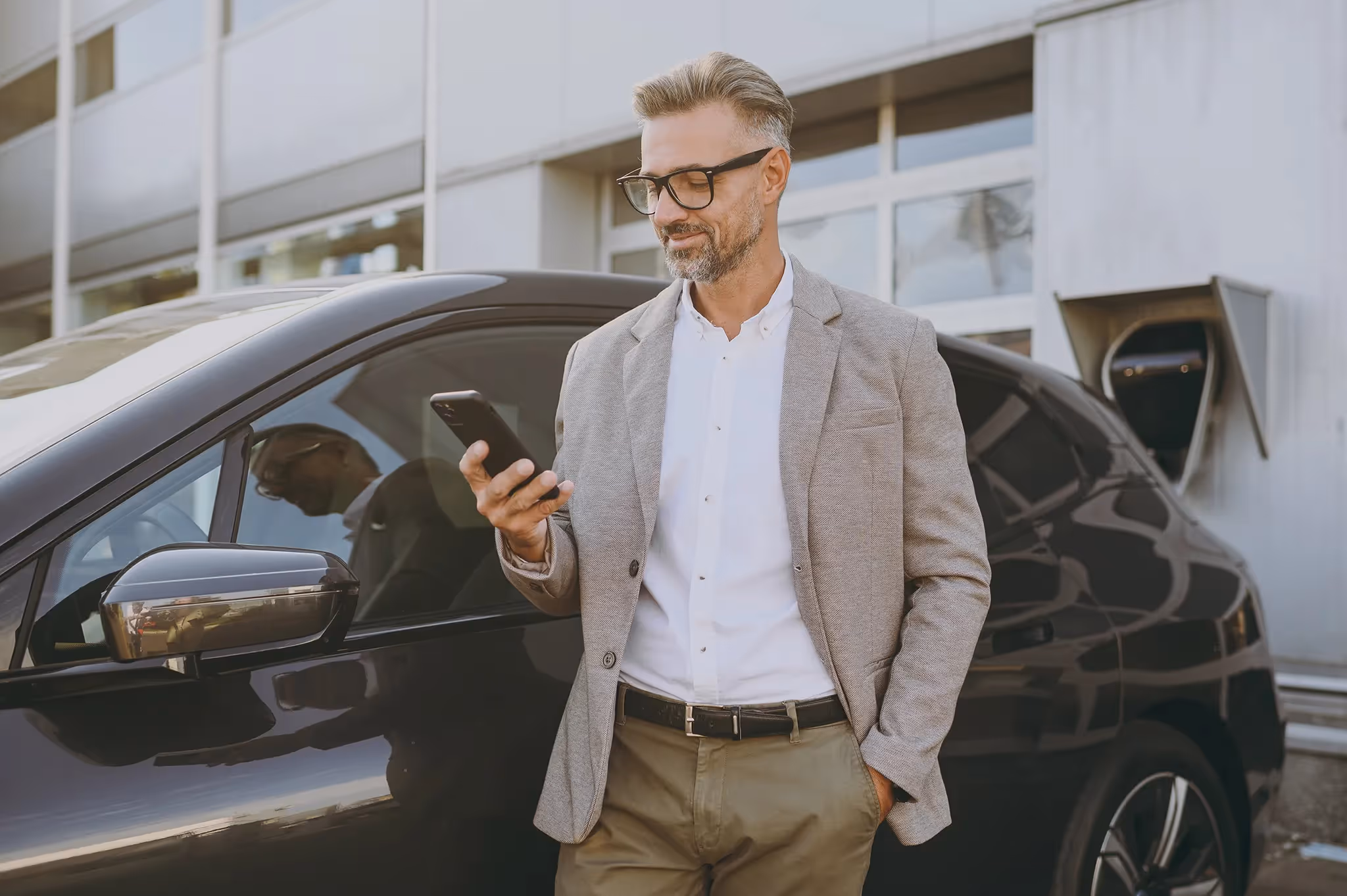 Older man standing next to black car looking at his cellphone