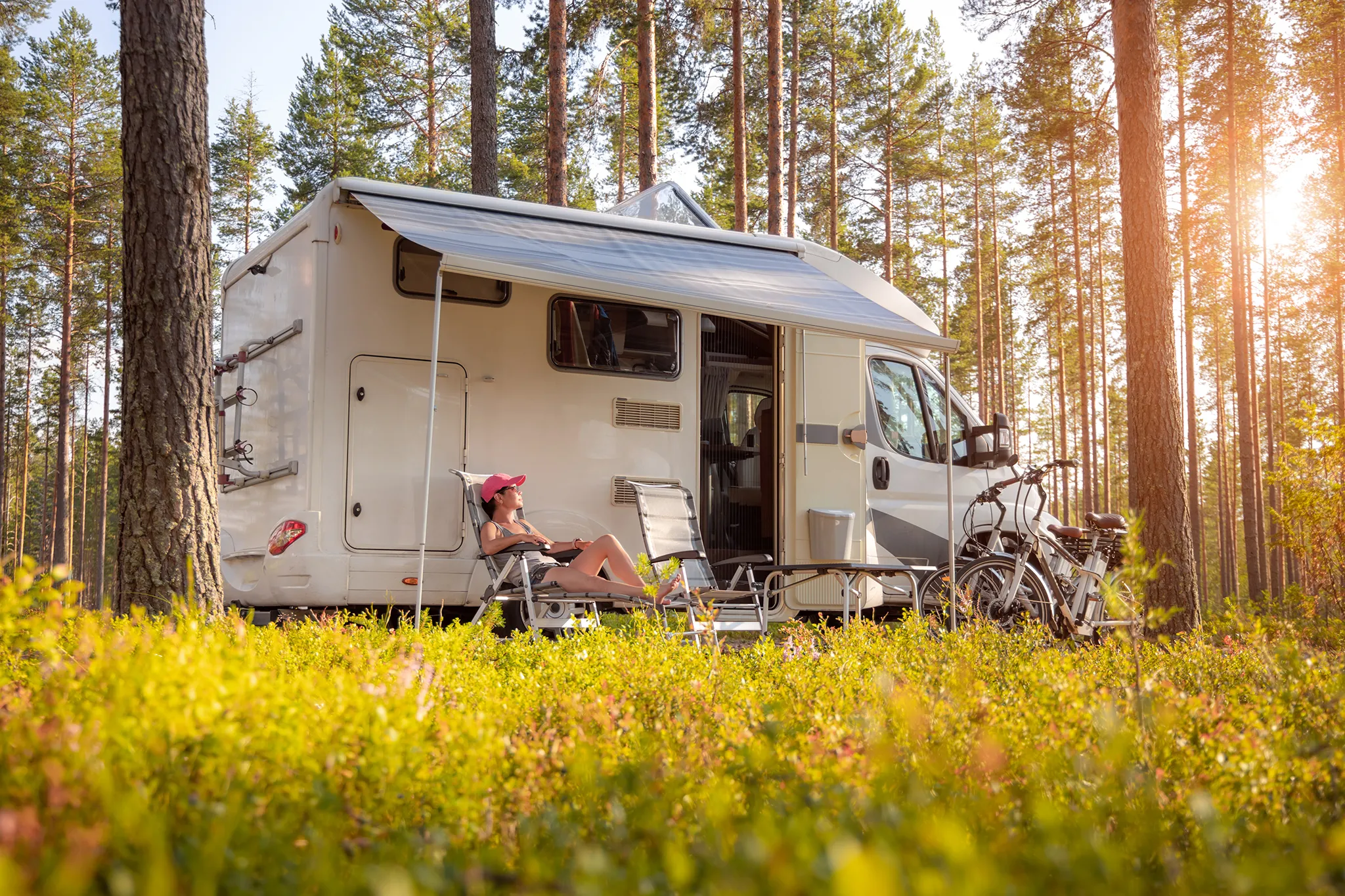 Woman sitting in lawnchair next to her campervan or motorhome in a forest setting