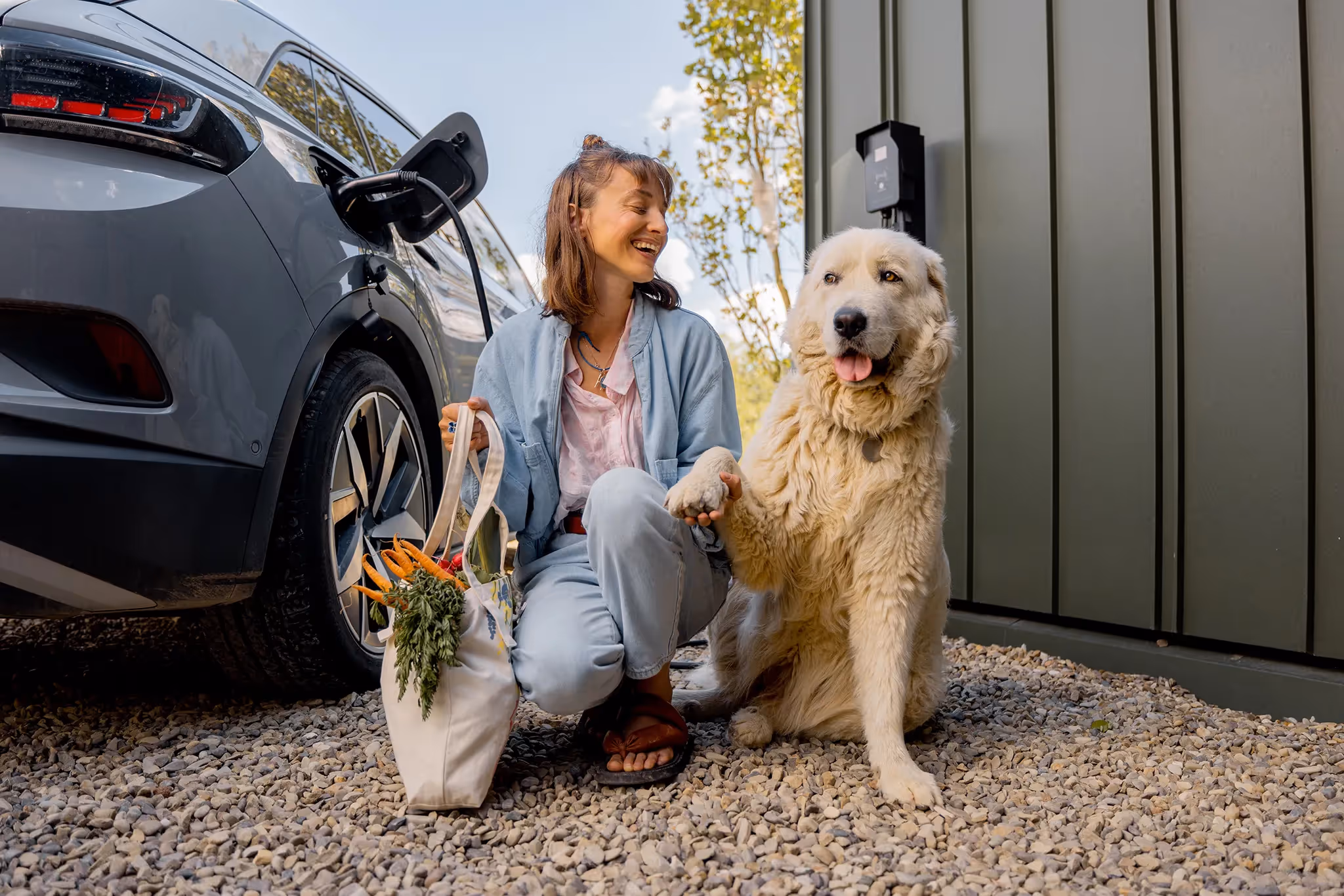 Young woman with her dog and a bag of fresh vegetables waiting for her electric car to recharge
