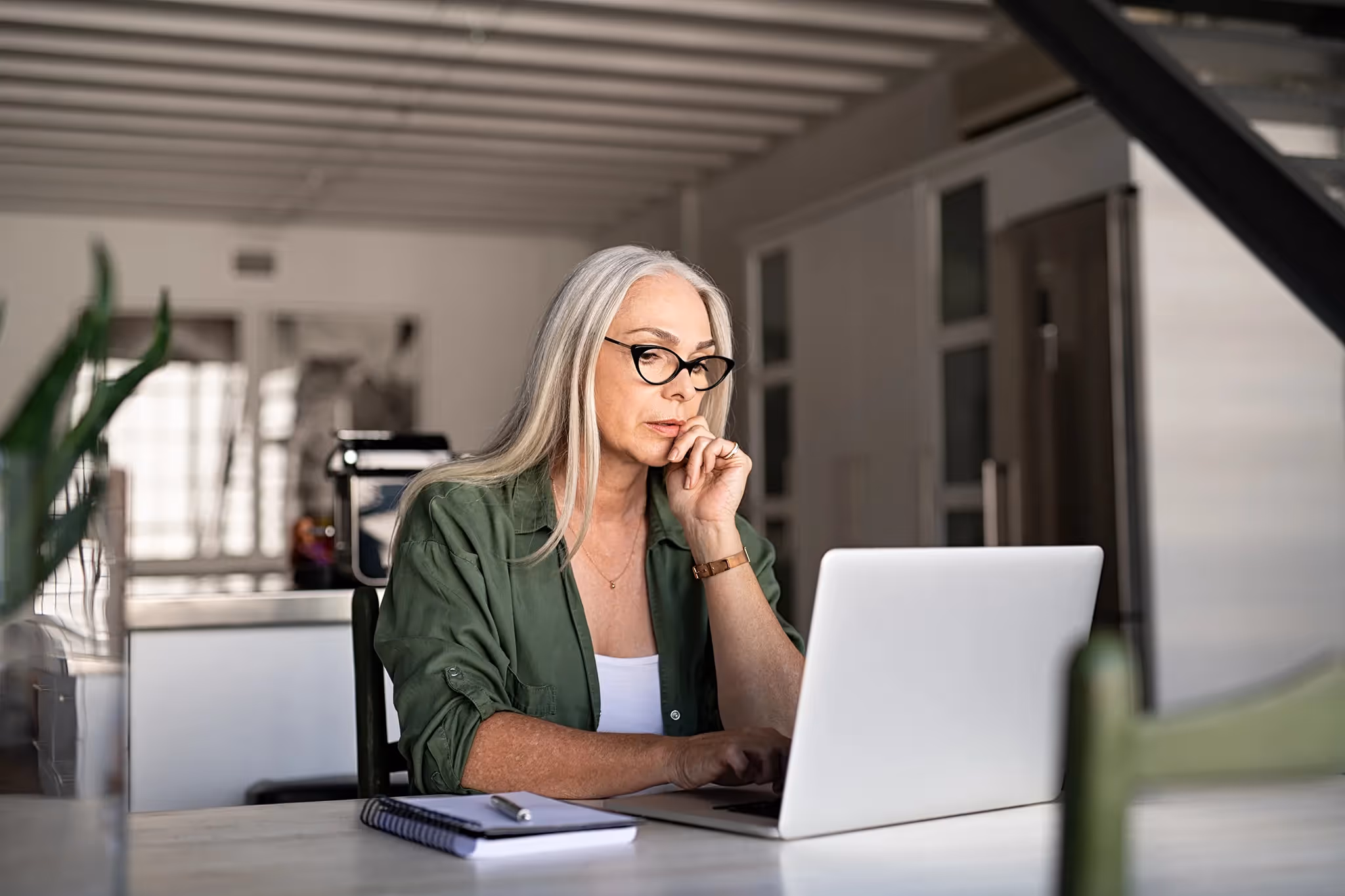 Mature woman working on laptop with notebook next to it, considering Term Life Insurance options