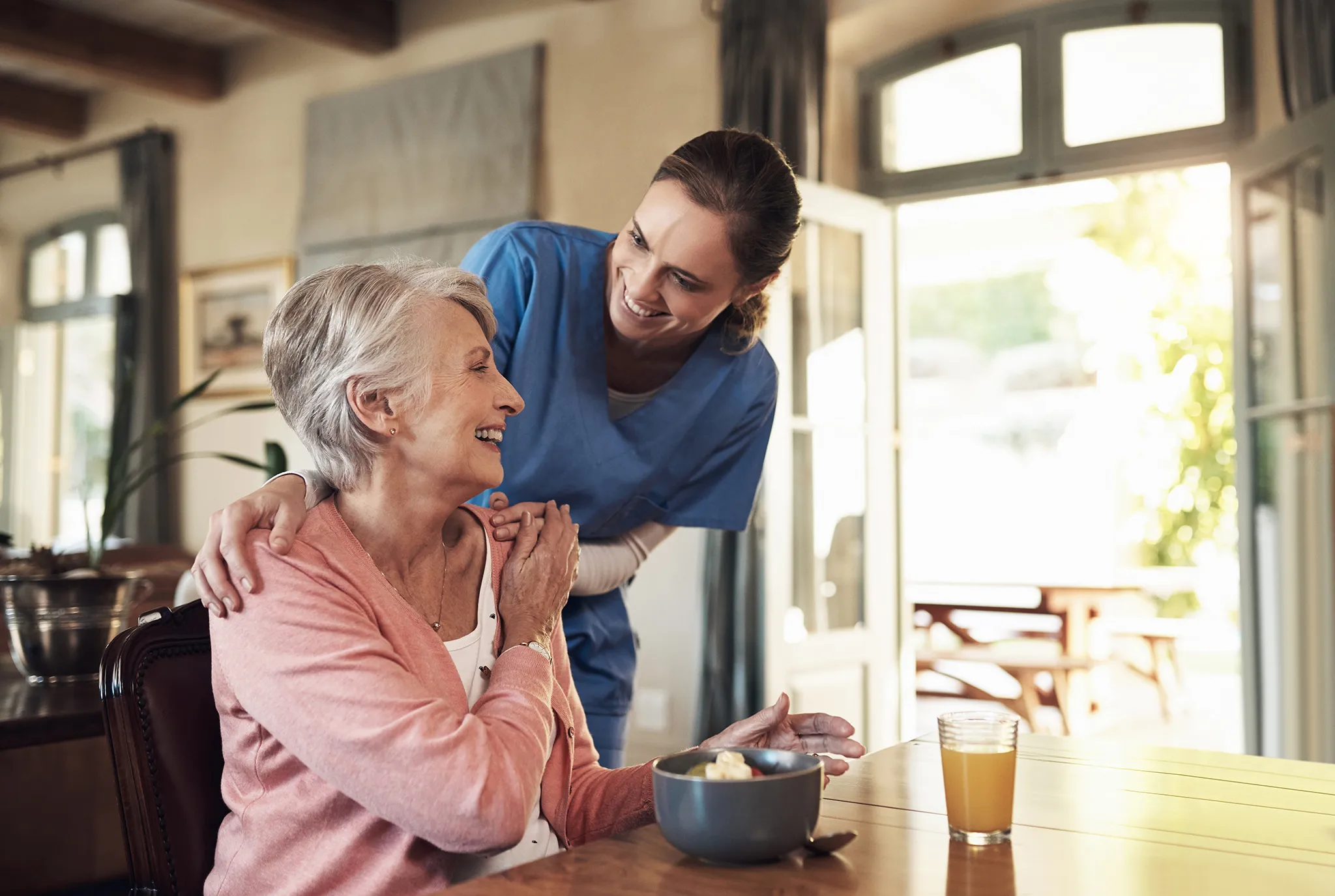 Young nurse smiling at a mature woman who is smiling while eating breakfast