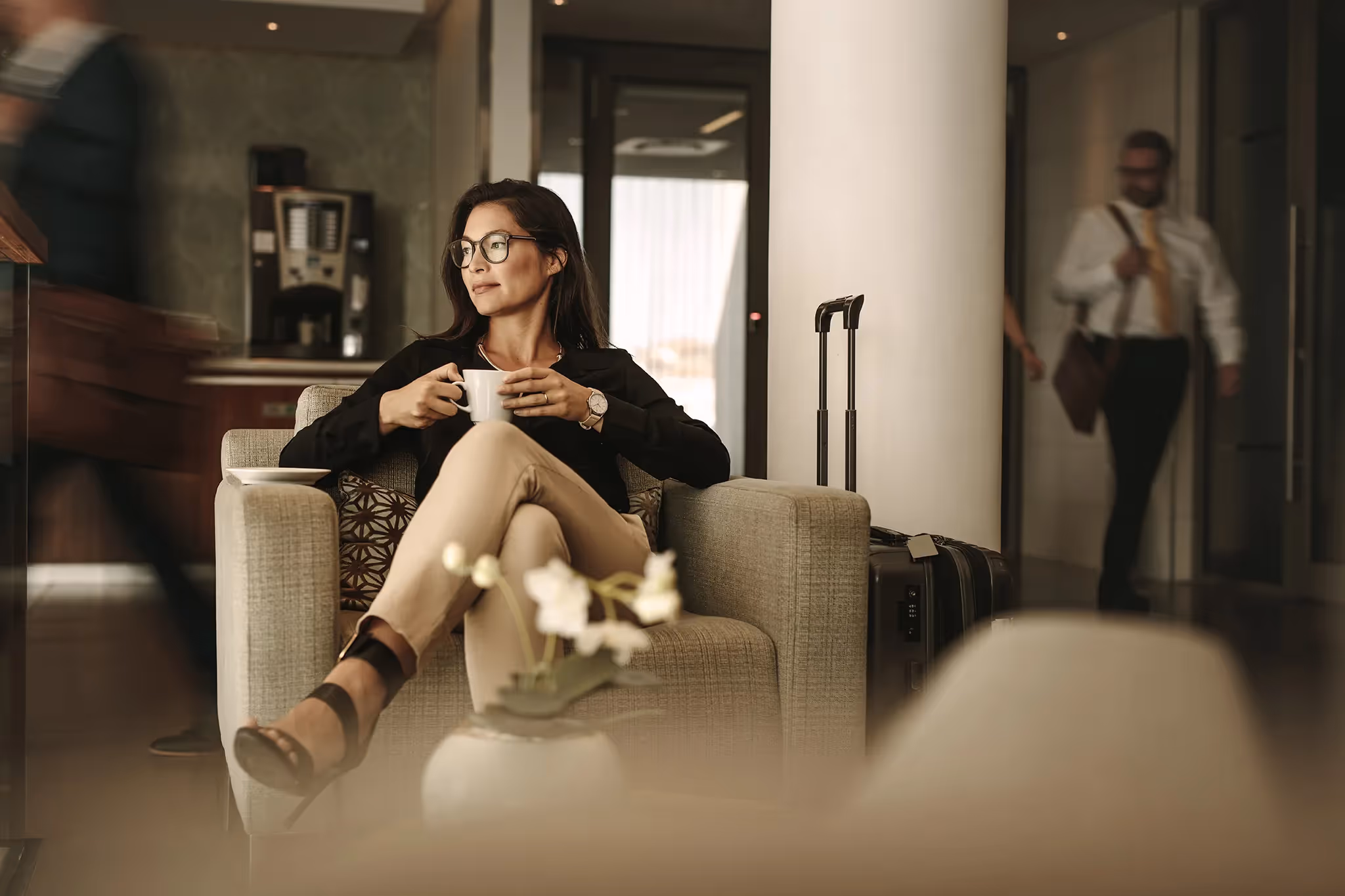 Businesswoman sitting in hotel lobby drinking coffee next to her suitcase with text Excess Liability and Personal Umbrella