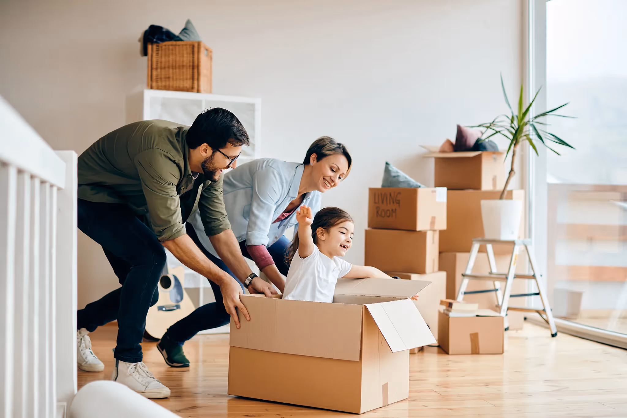 Happy parents playing with young daughter surrounded by moving boxes