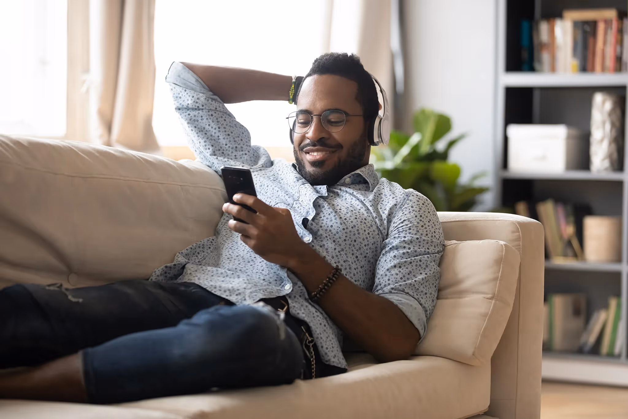 Man in his thirties listening to music and scrolling on his phone on a couch in his apartment