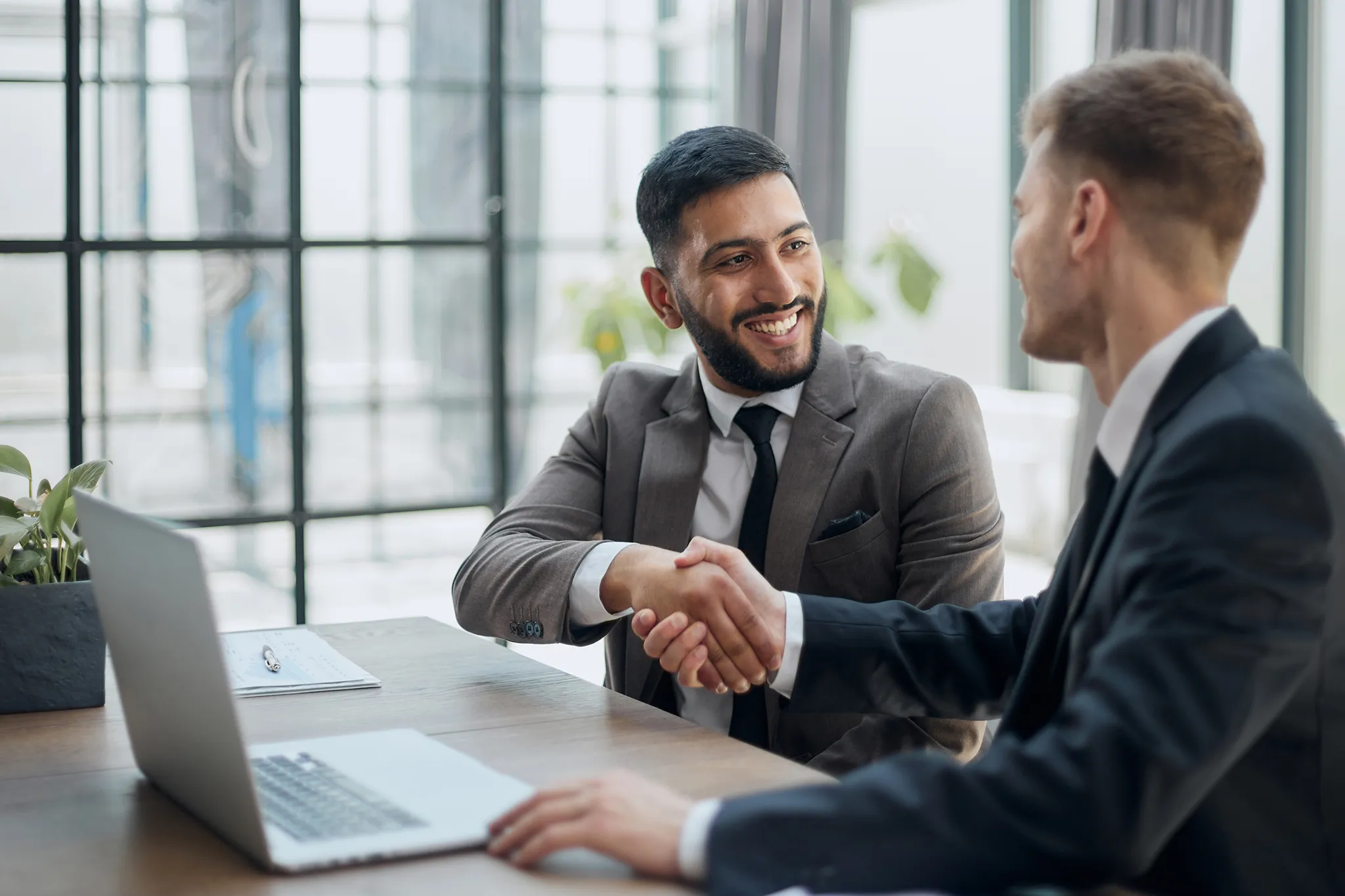 Bearded young businessman shaking hands with another businessman at a table in a meeting room