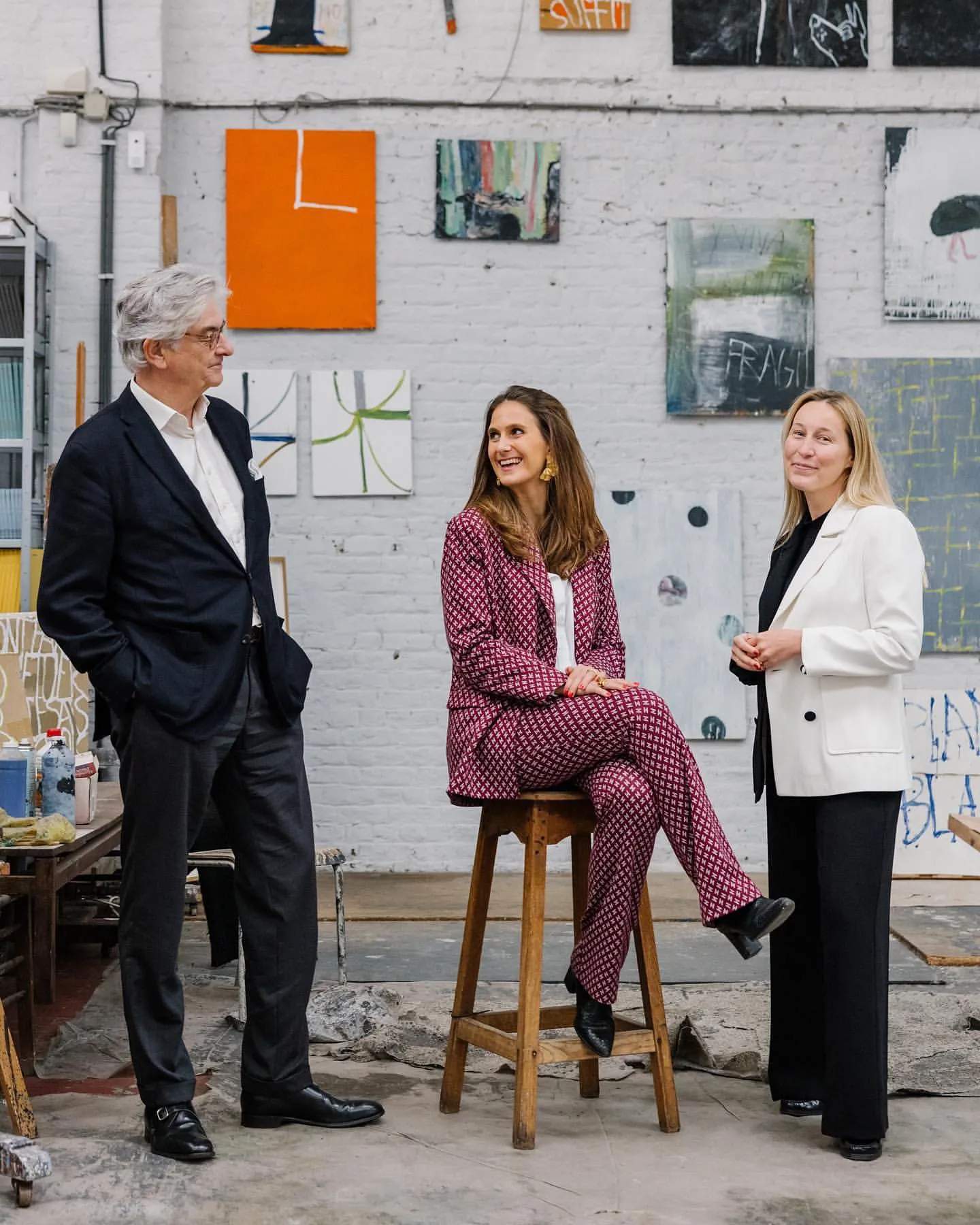 Three people smiling and posing for a picture in a room filled with paintings
