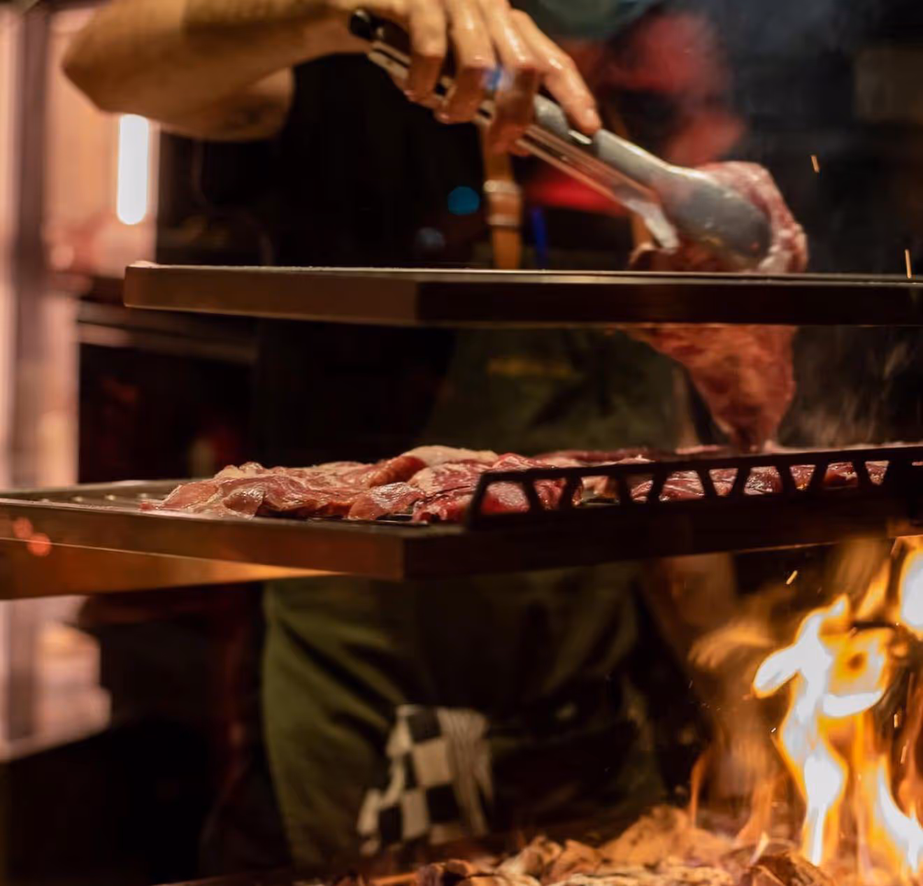 Someone turning a piece of meat above a grill