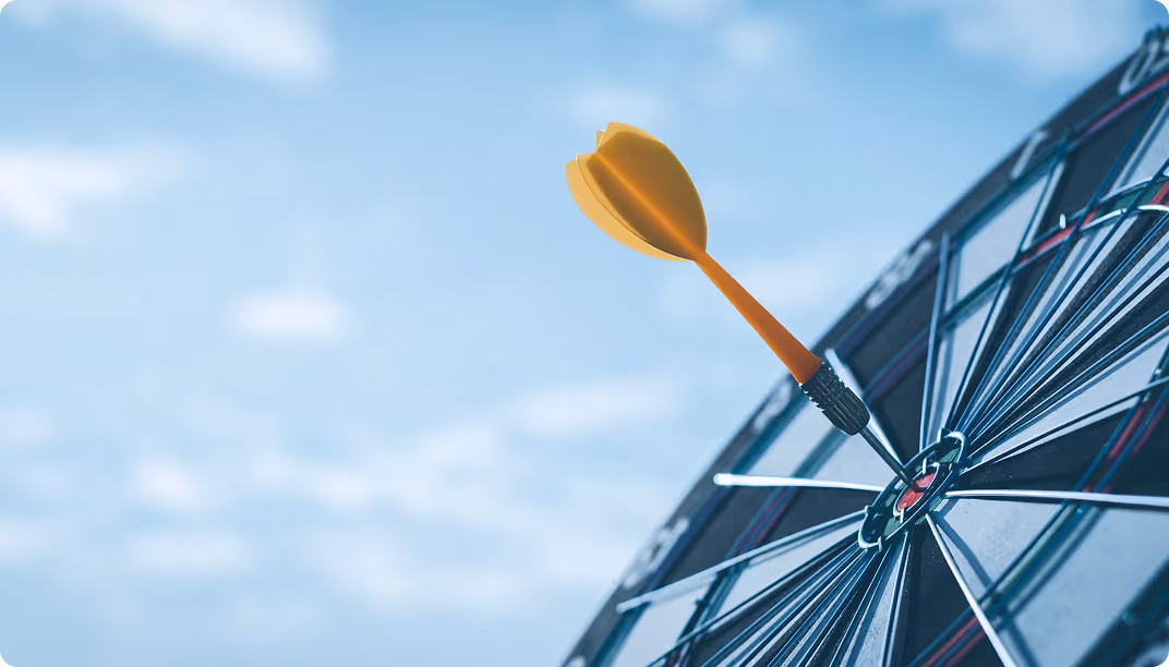 Yellow dart hitting the bullseye on a dartboard with a blue sky background
