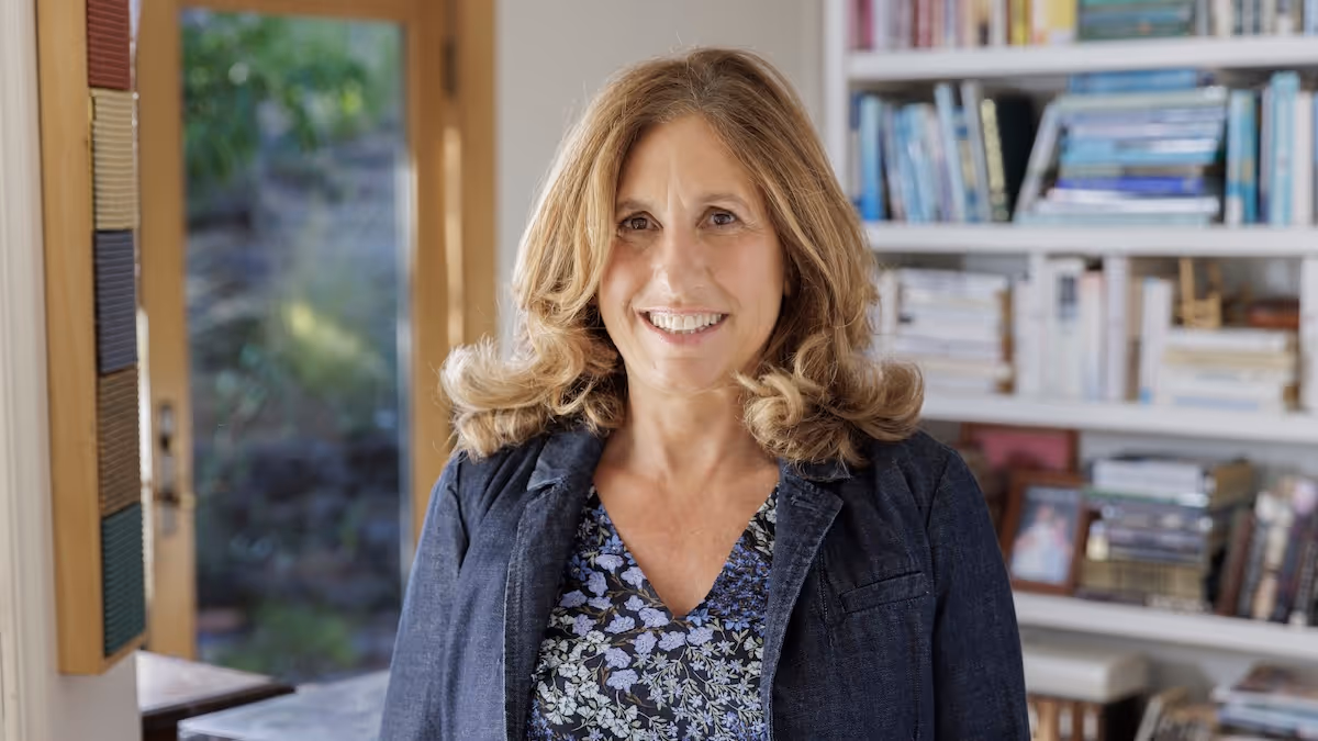 Lisa tabb, smiling to camera wearing a smart jacket, infront of an informal bookcase
