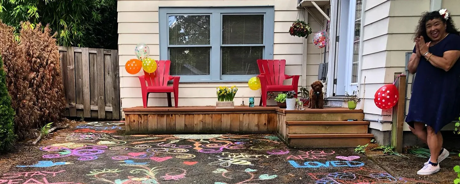 Mary from Paradym Events standing beside a colorful event setup featuring sidewalk chalk art, floral arrangements, and balloons