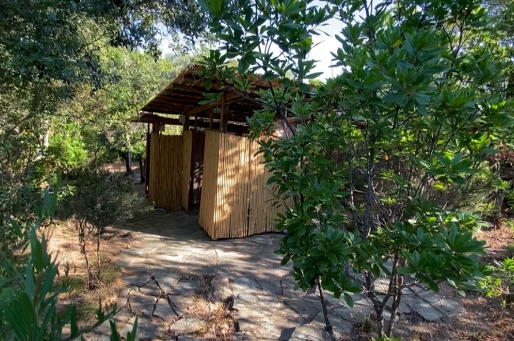 Wooden outdoor showers with bamboo walls surrounded by dense green foliage and stone pathway.