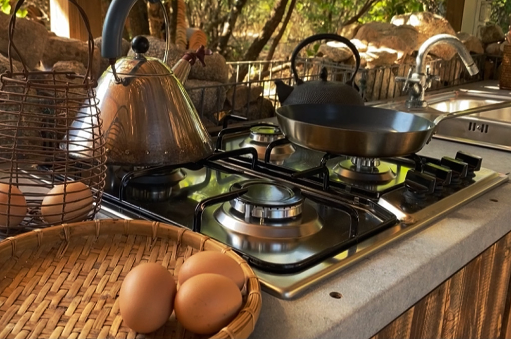 Kitchen stove with a metal kettle, frying pan, wire basket with eggs, and a woven basket with eggs on the countertop.
