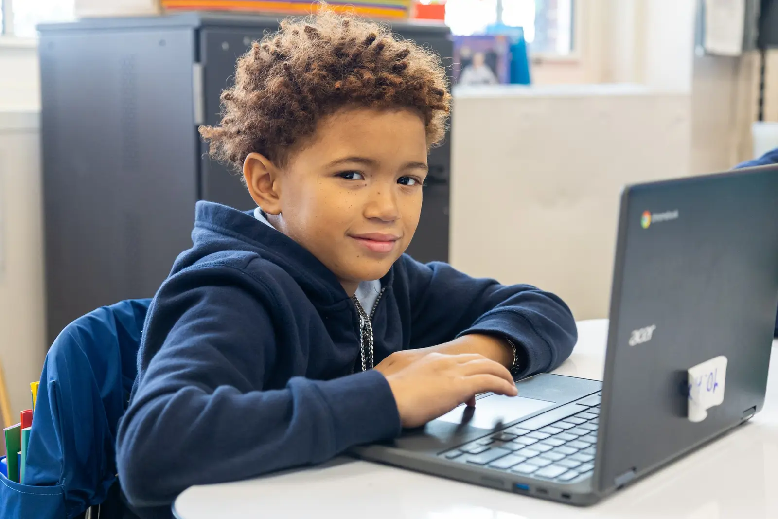 Student smiling while working on a Chromebook laptop in class