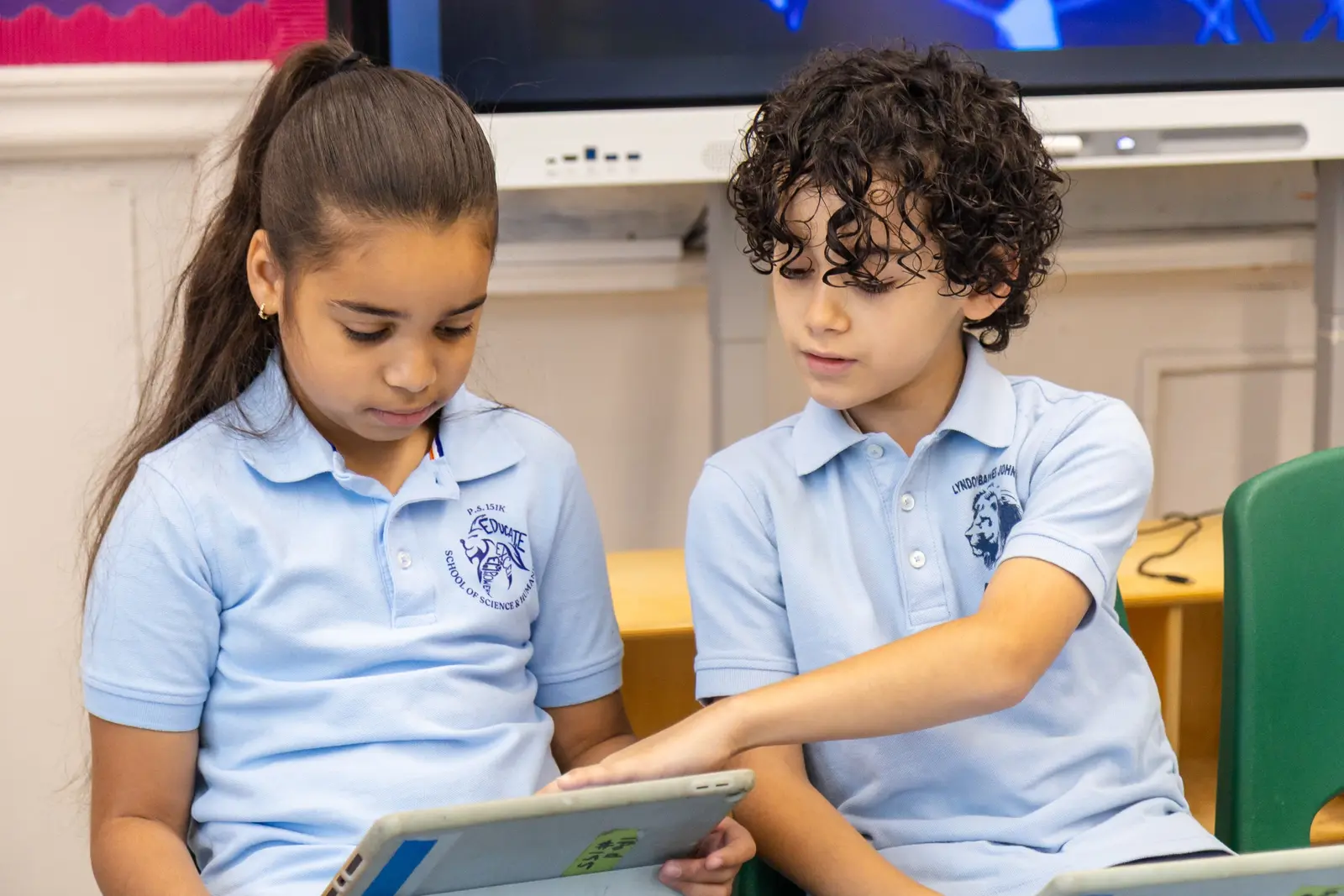 Two students in uniform collaborating on a tablet in class
