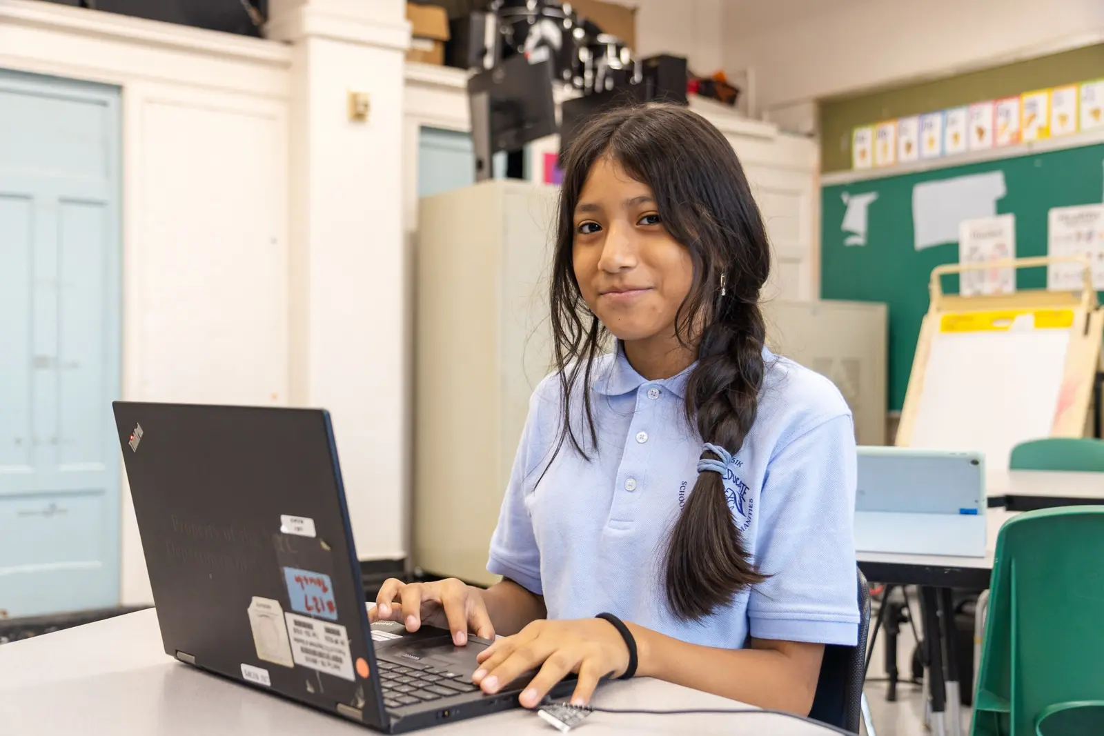 Student in school uniform smiling while working on laptop in classroom