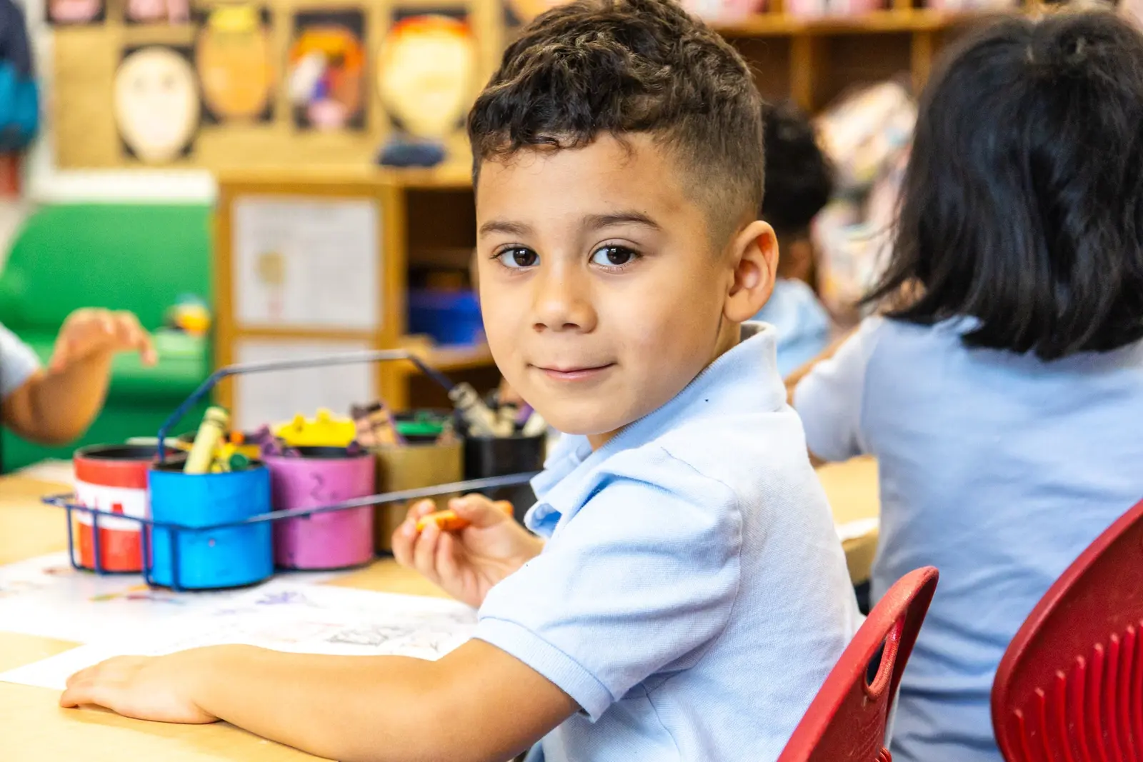 Young student smiling while coloring with crayons in classroom
