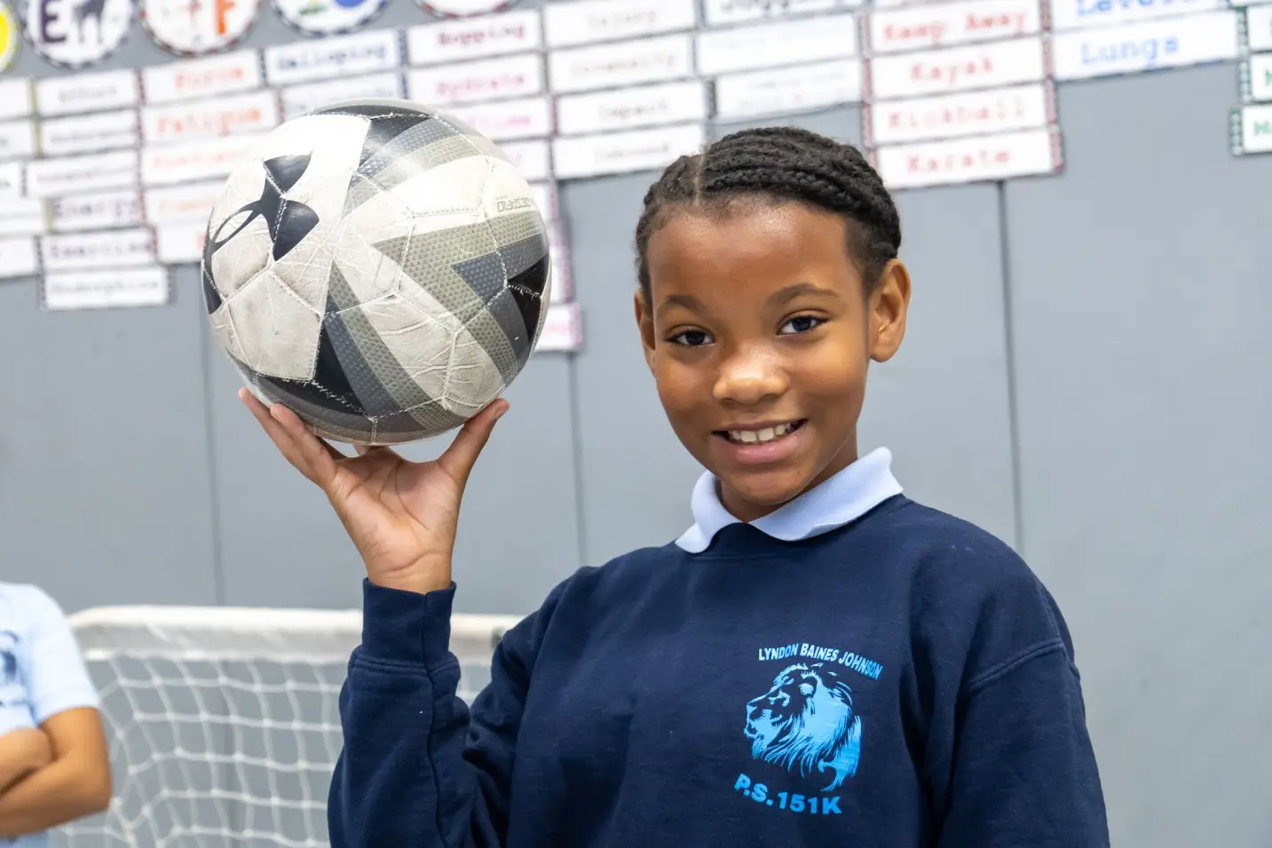 Student in school uniform holding a football and smiling in classroom
