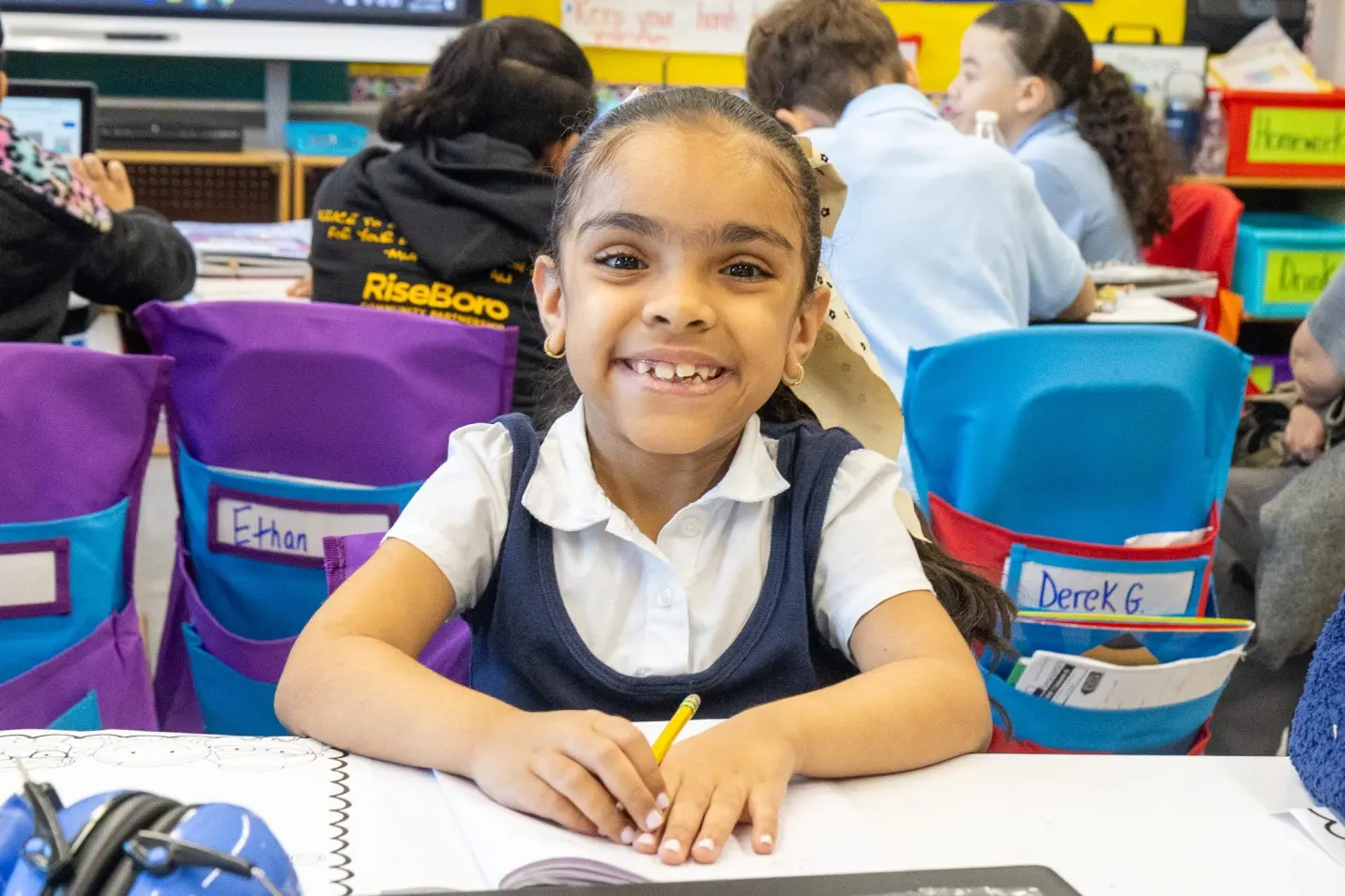 Smiling student in uniform writing at her classroom desk