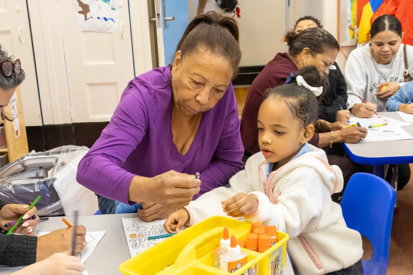 Adult helping young student with a coloring craft activity in classroom