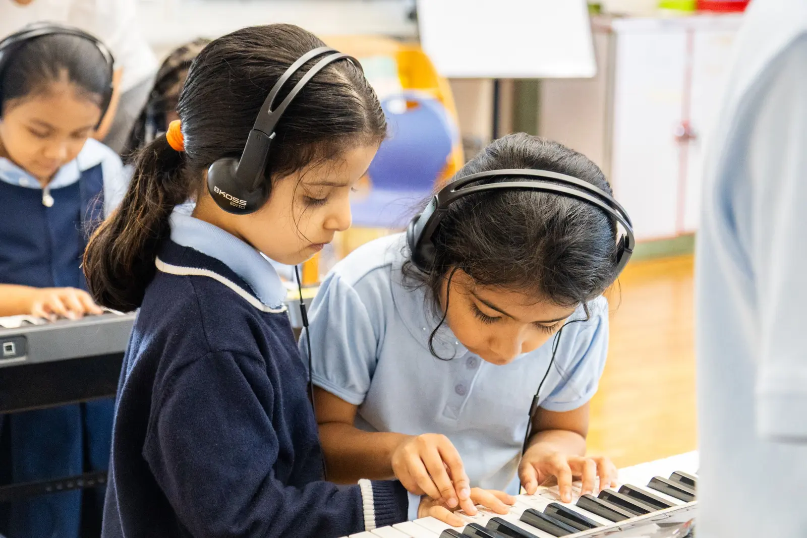 Two students wearing headphones playing keyboard together in music class