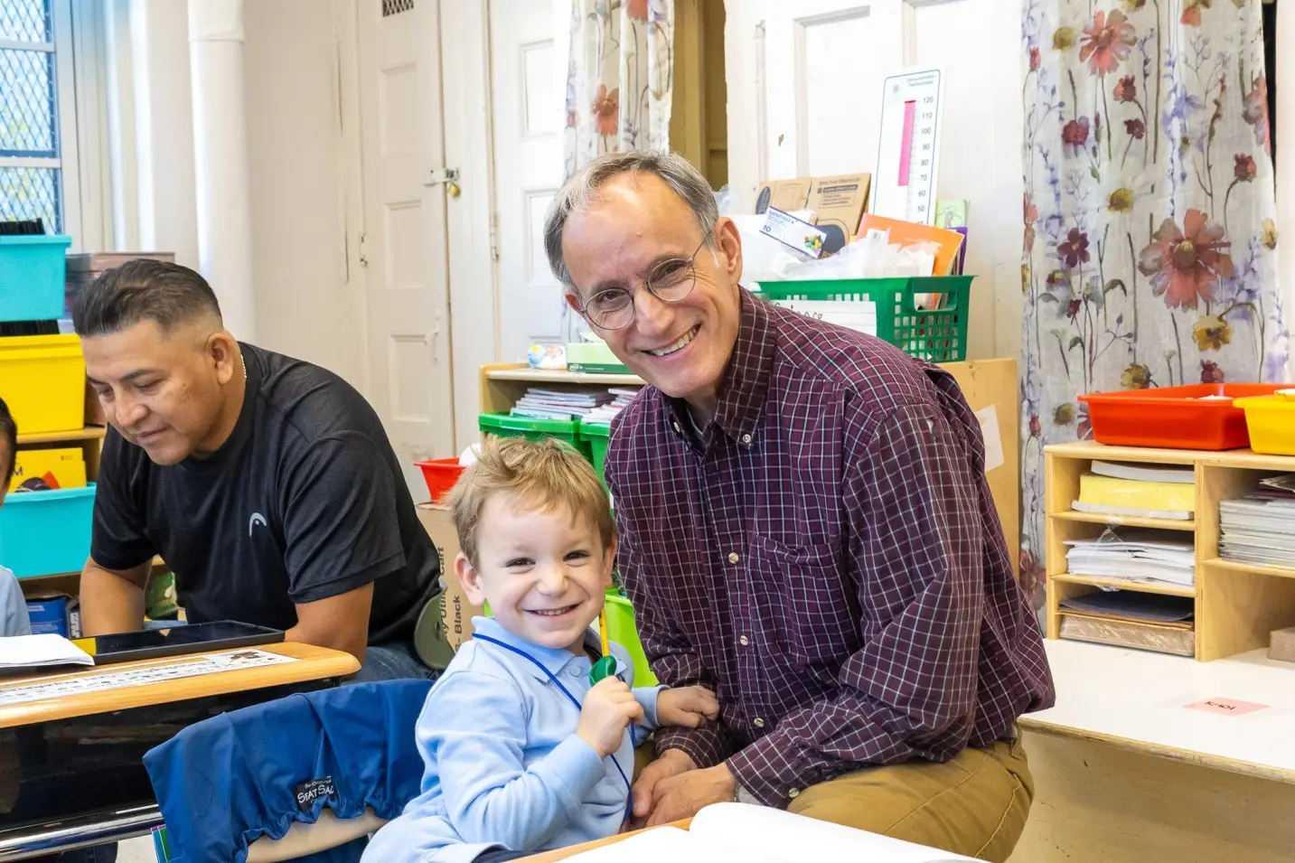 Adult visitor smiling with young student at classroom desk