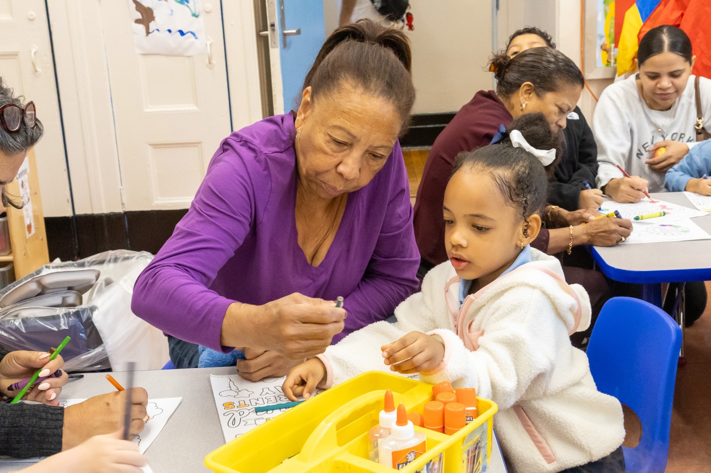 Adult helping a young student with a classroom art activity