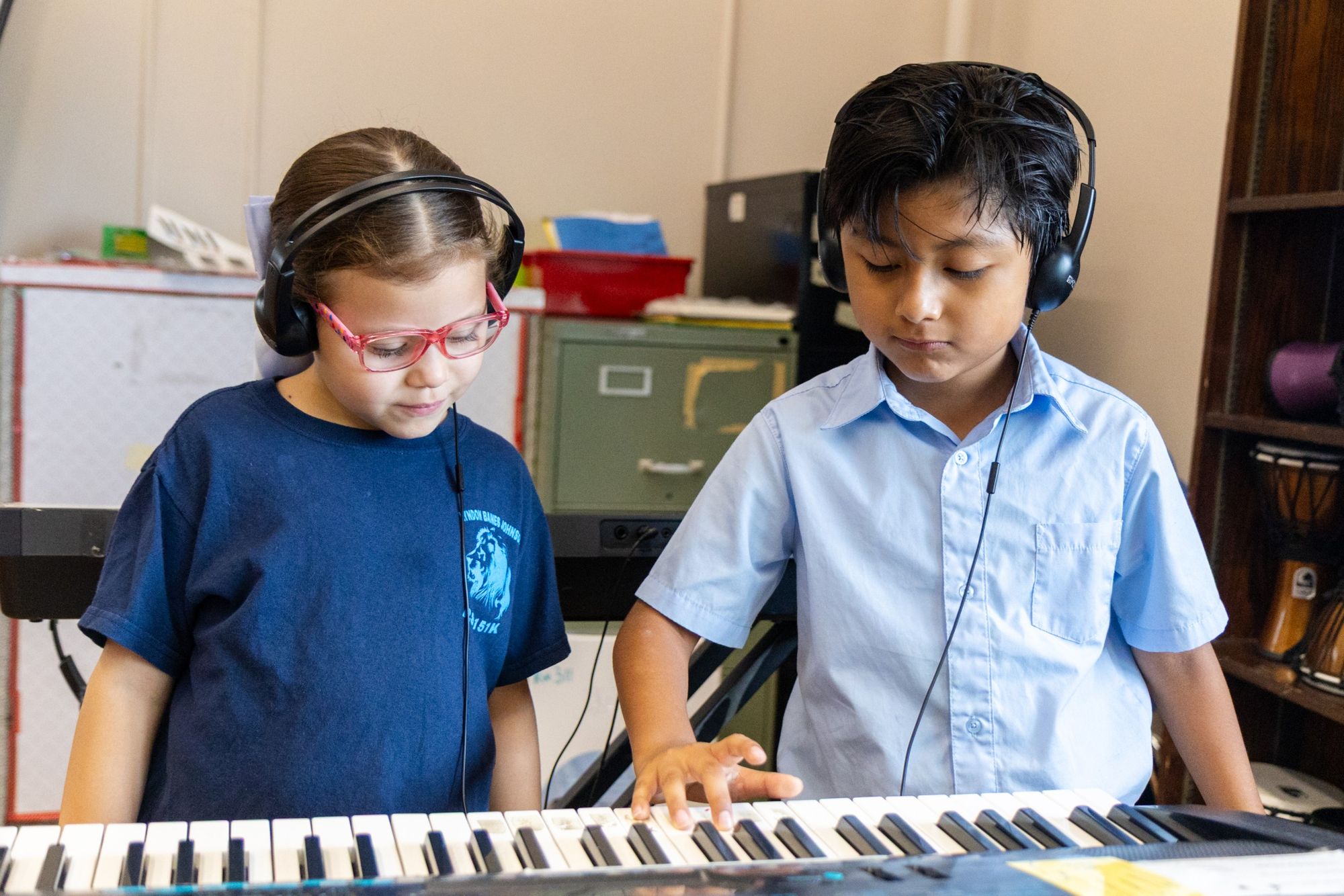 Two students wearing headphones play keyboard together in music class