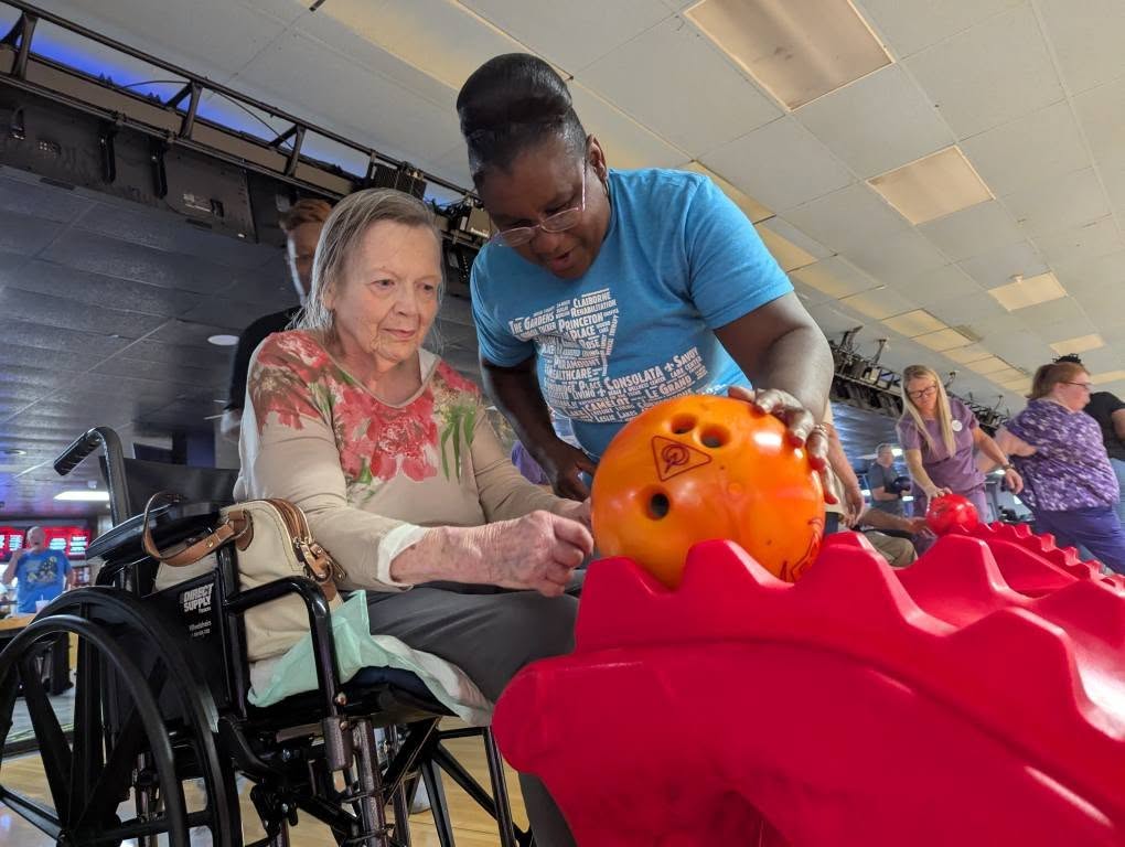 Nurse assisting a resident with rolling a bowling ball