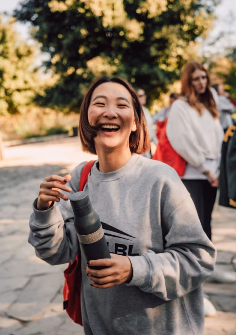 Lu Zhang smiling with a grey sweatshirt on holding a water bottle