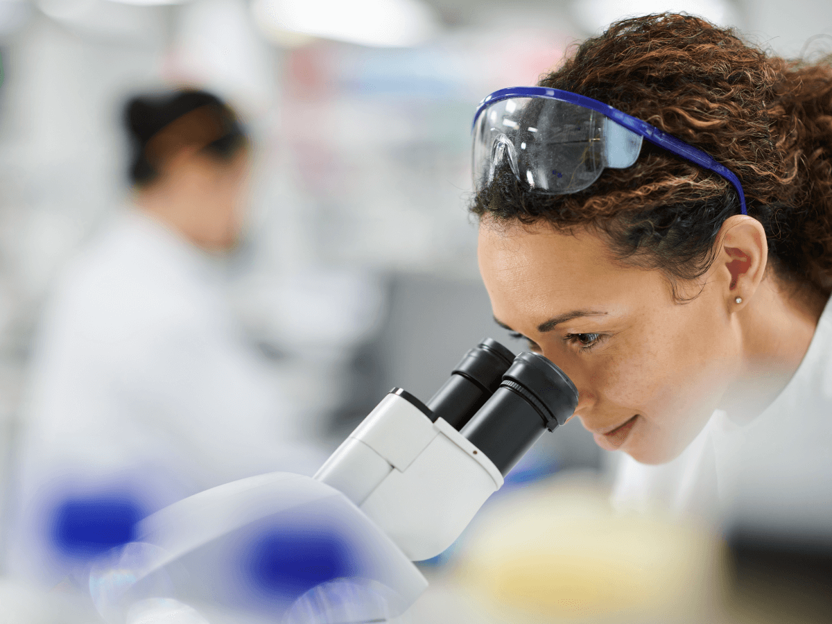 A woman in a lab peers into a microscope.